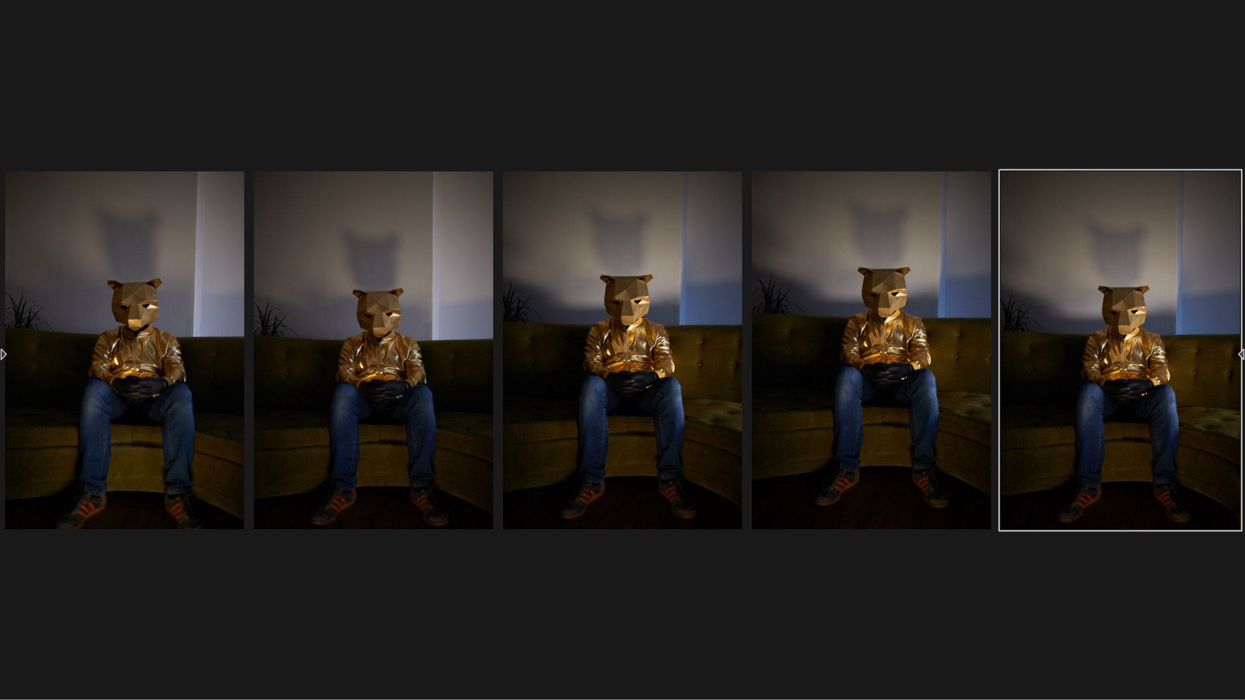 Person wearing a bear mask and gold jacket sitting on a green sofa, holding a phone, in a dimly lit room.