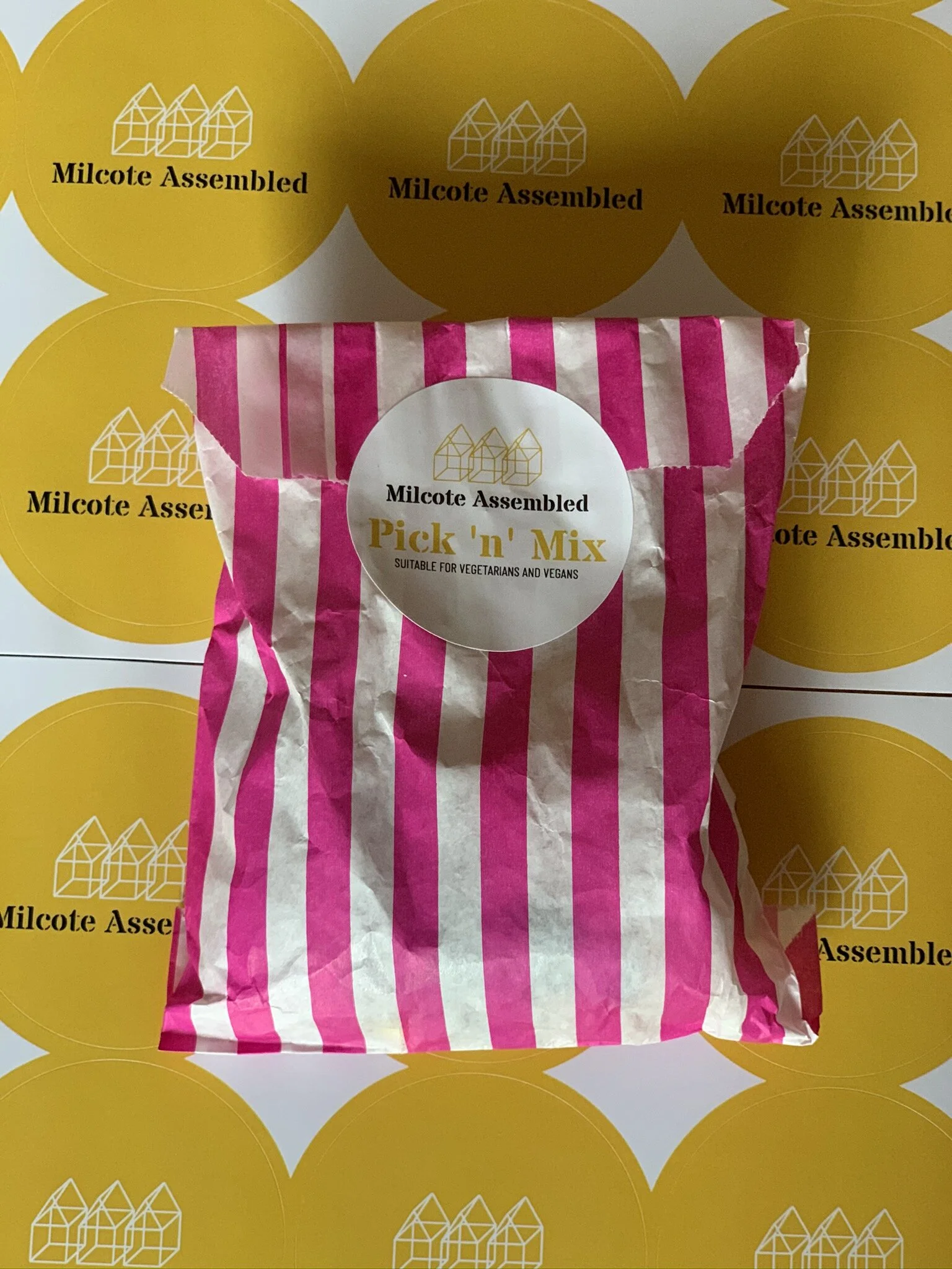 Pink and white striped bag of 'Pick 'n' Mix' candies on a yellow background with 