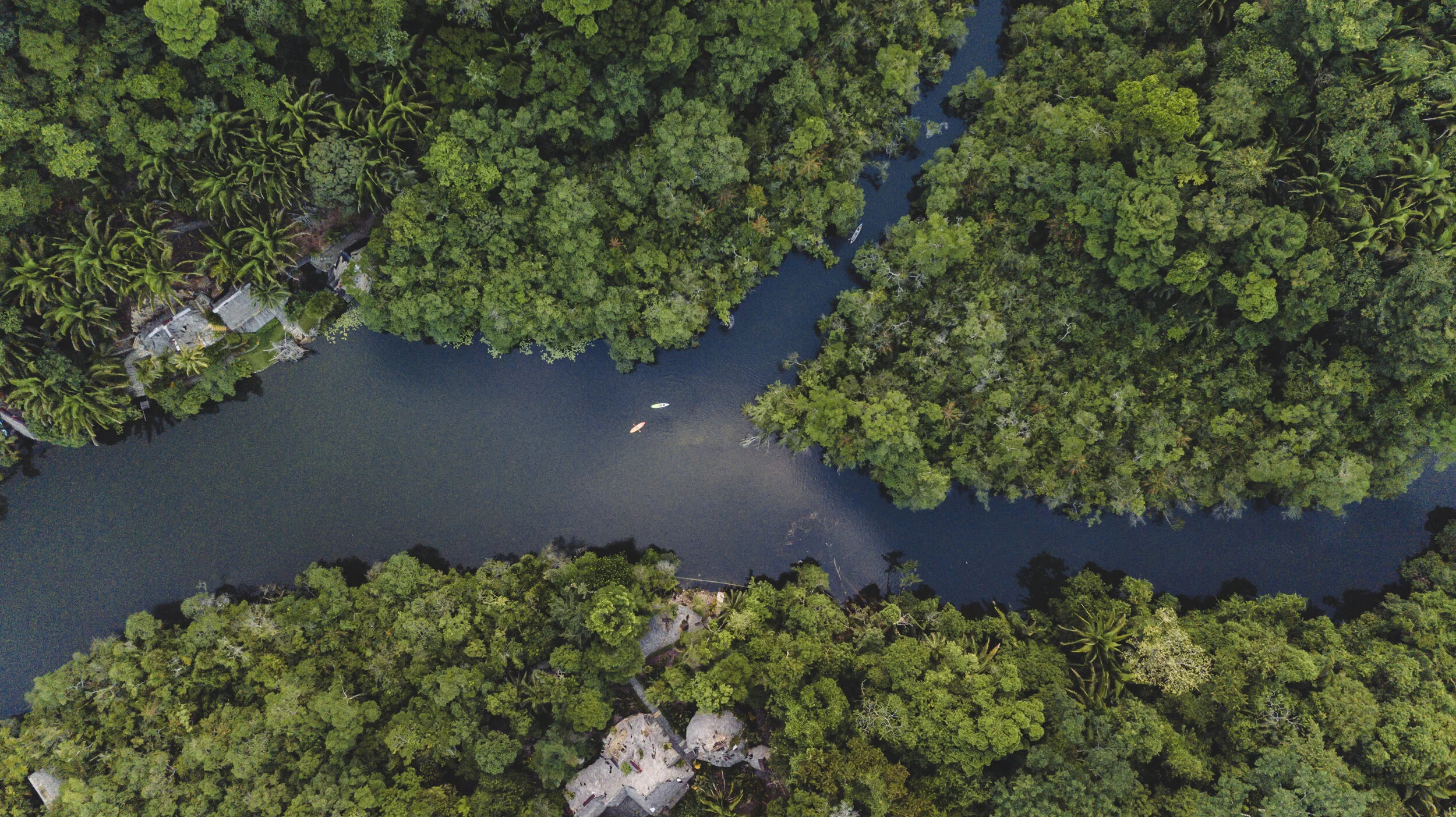 Bird's eye view of Rio Dulce Guatemala winding through a dense tropical forest with a few boats on the water and some small structures along the banks.