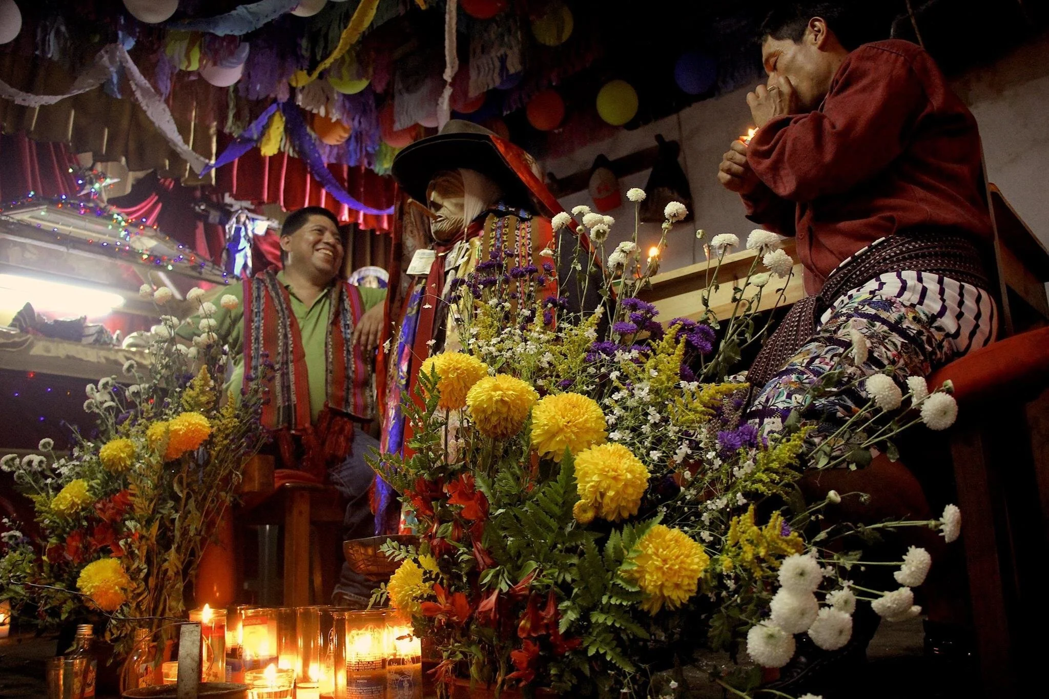 A vibrant celebration with two men wearing traditional Guatemalan clothing in the Maximon shrine
