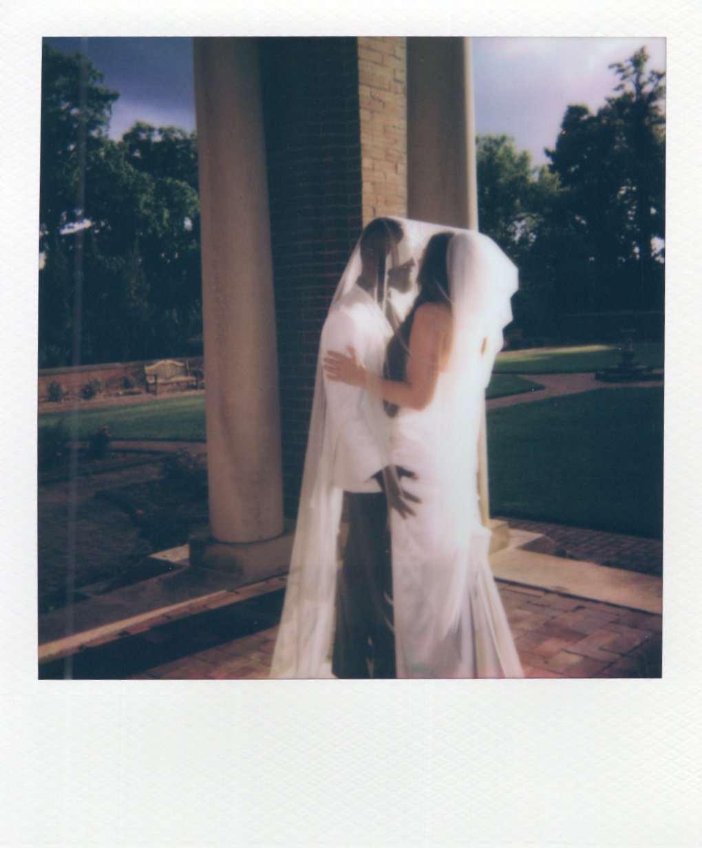 Polaroid of couple leaning in to kiss underneath the bride's veil