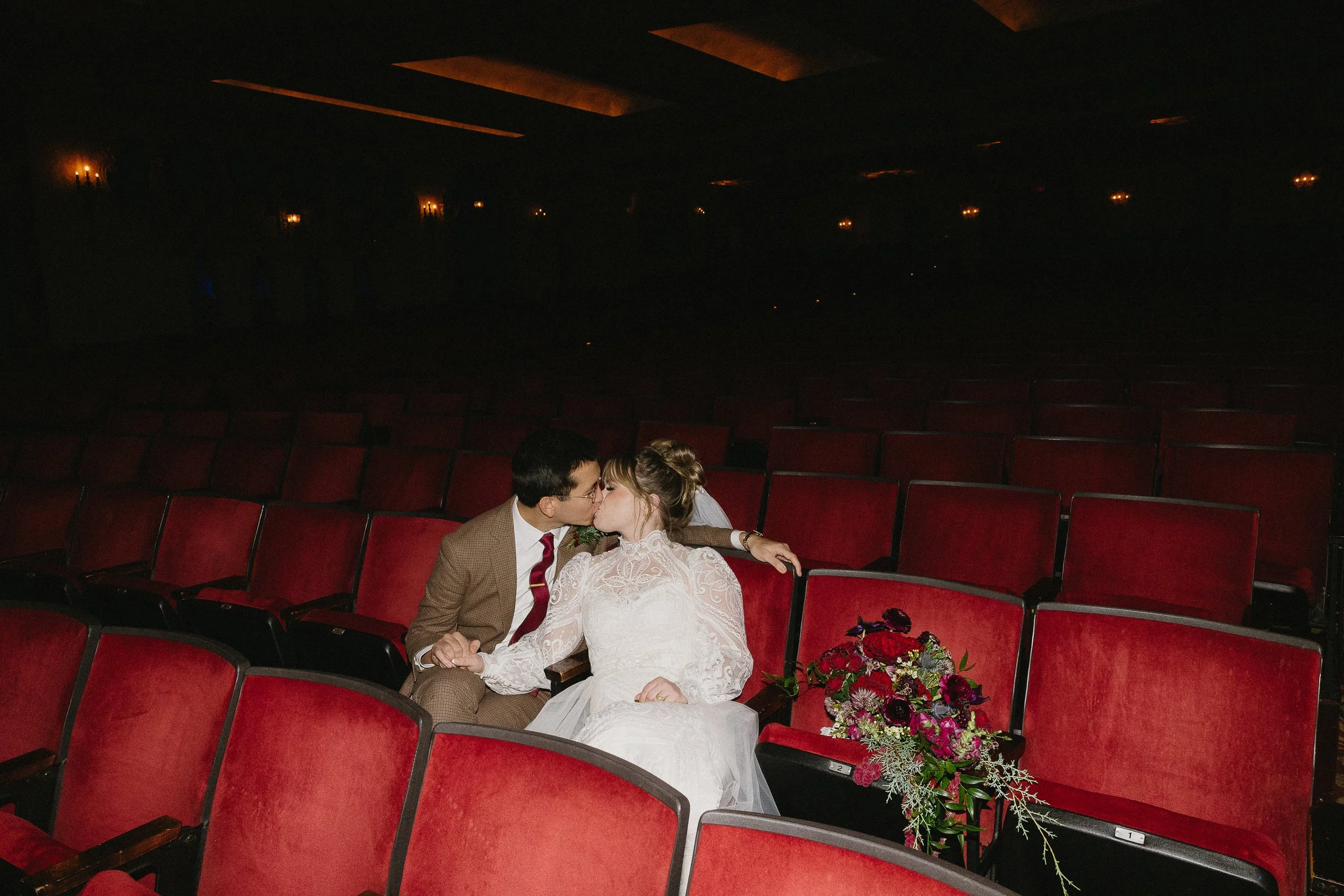 Moody shot of a couple kissing on their wedding day in a red theatre