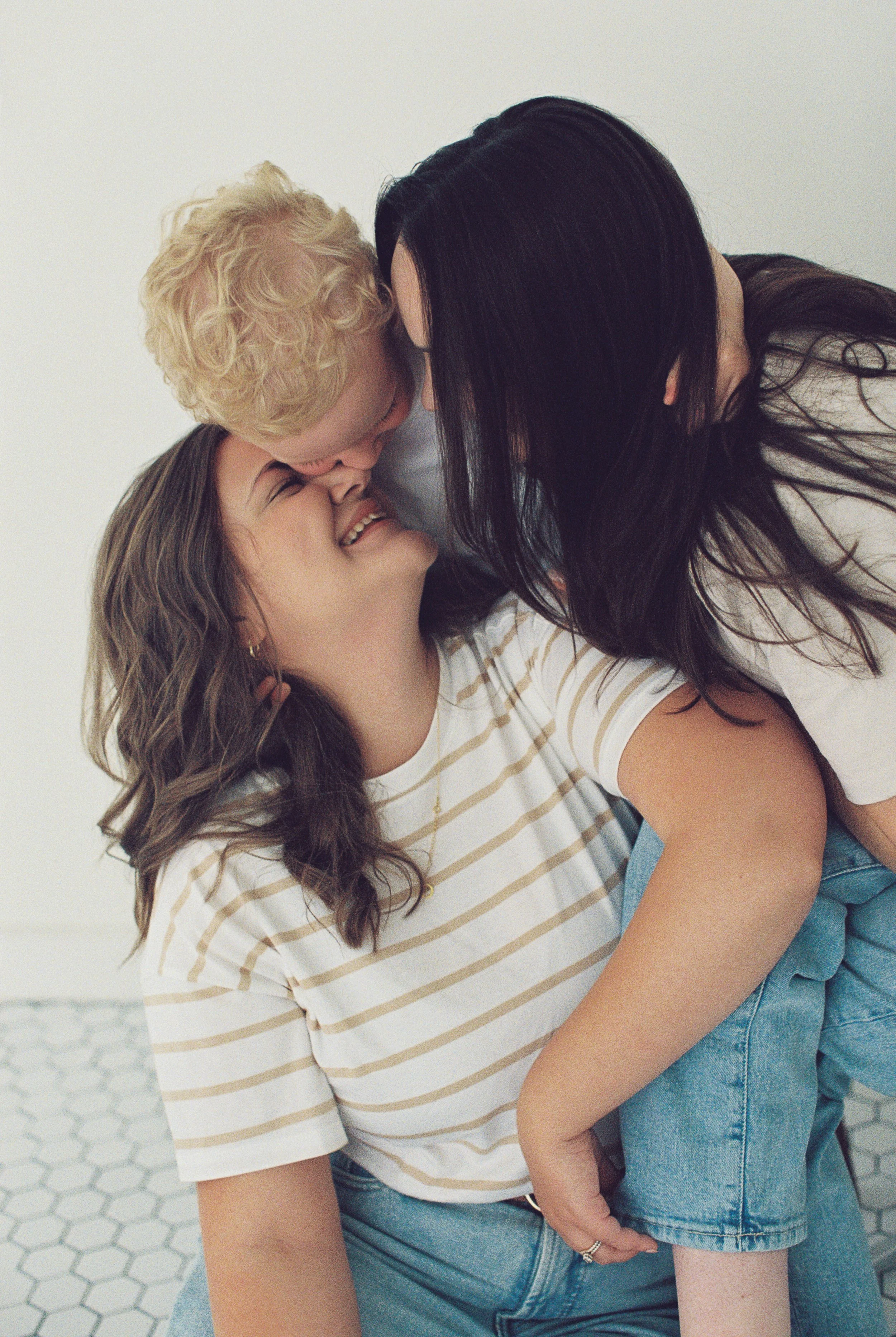 Two women happily snuggling a young kid in the center