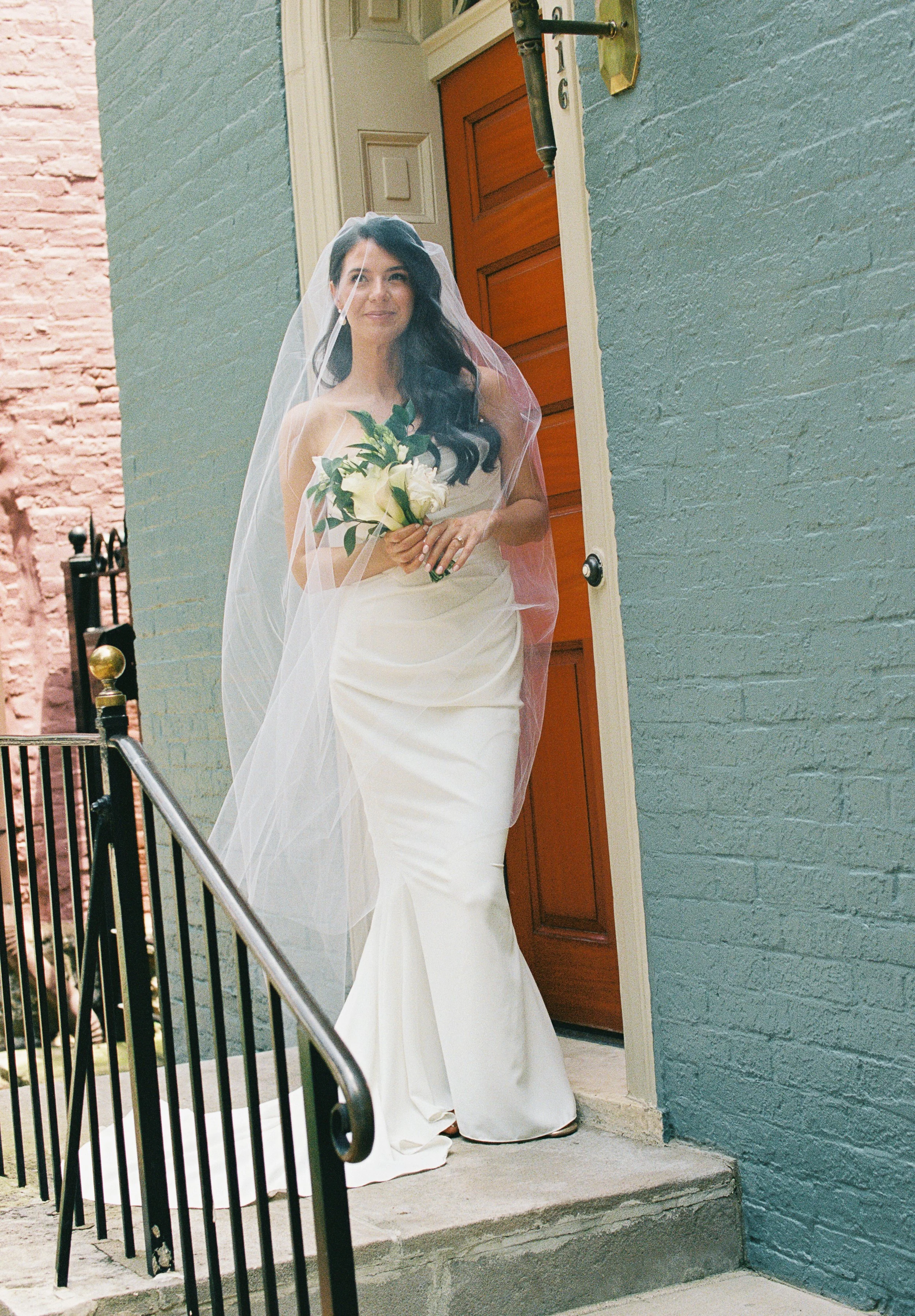 Beautiful bridge walking down a staircase with her bouquet and veil pulled forward