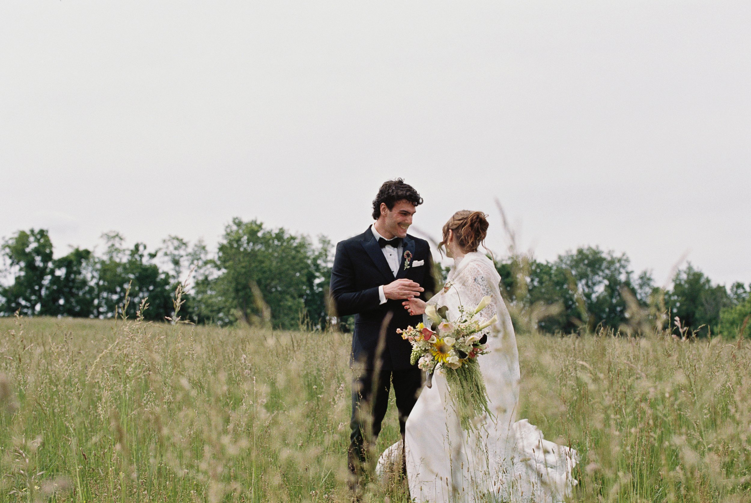 Bride and Groom standing in a field together in their wedding attire