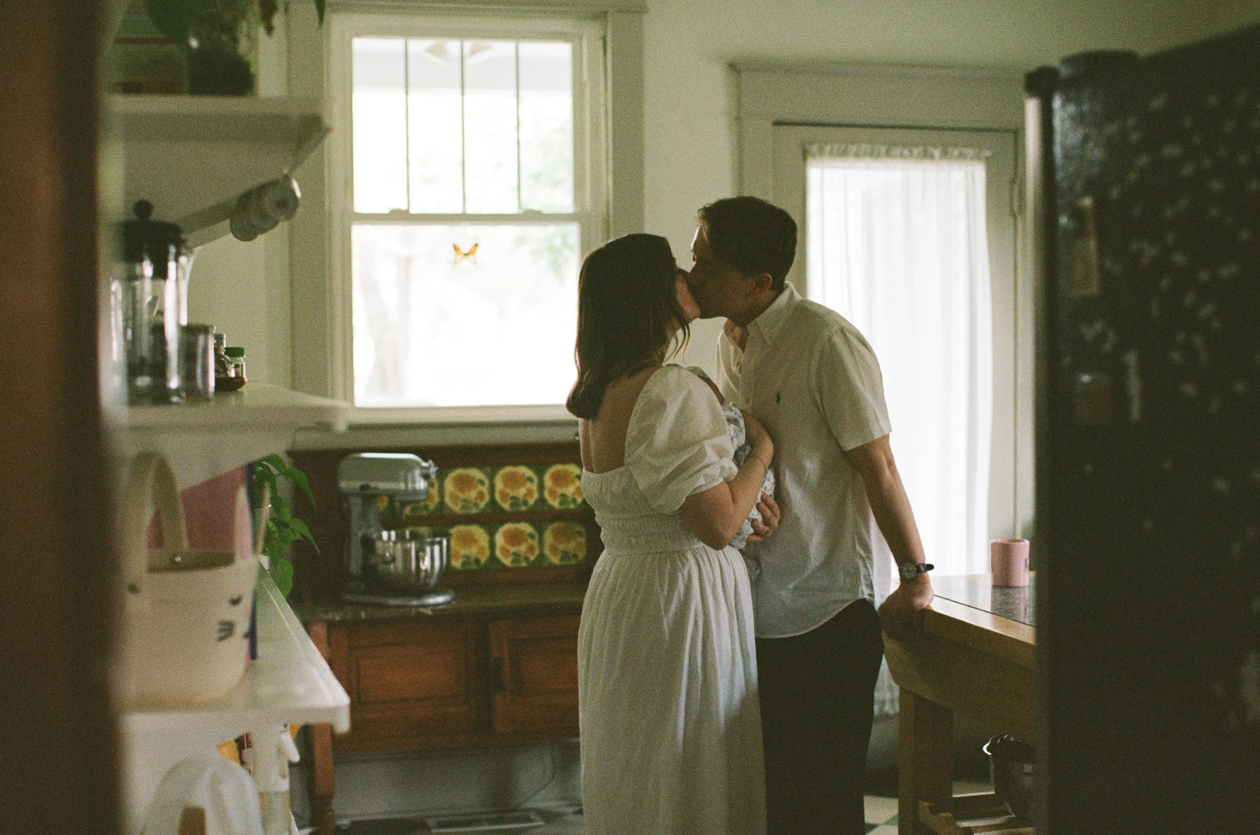 Couple holding their new baby close to their chest as they lean in to kiss each other