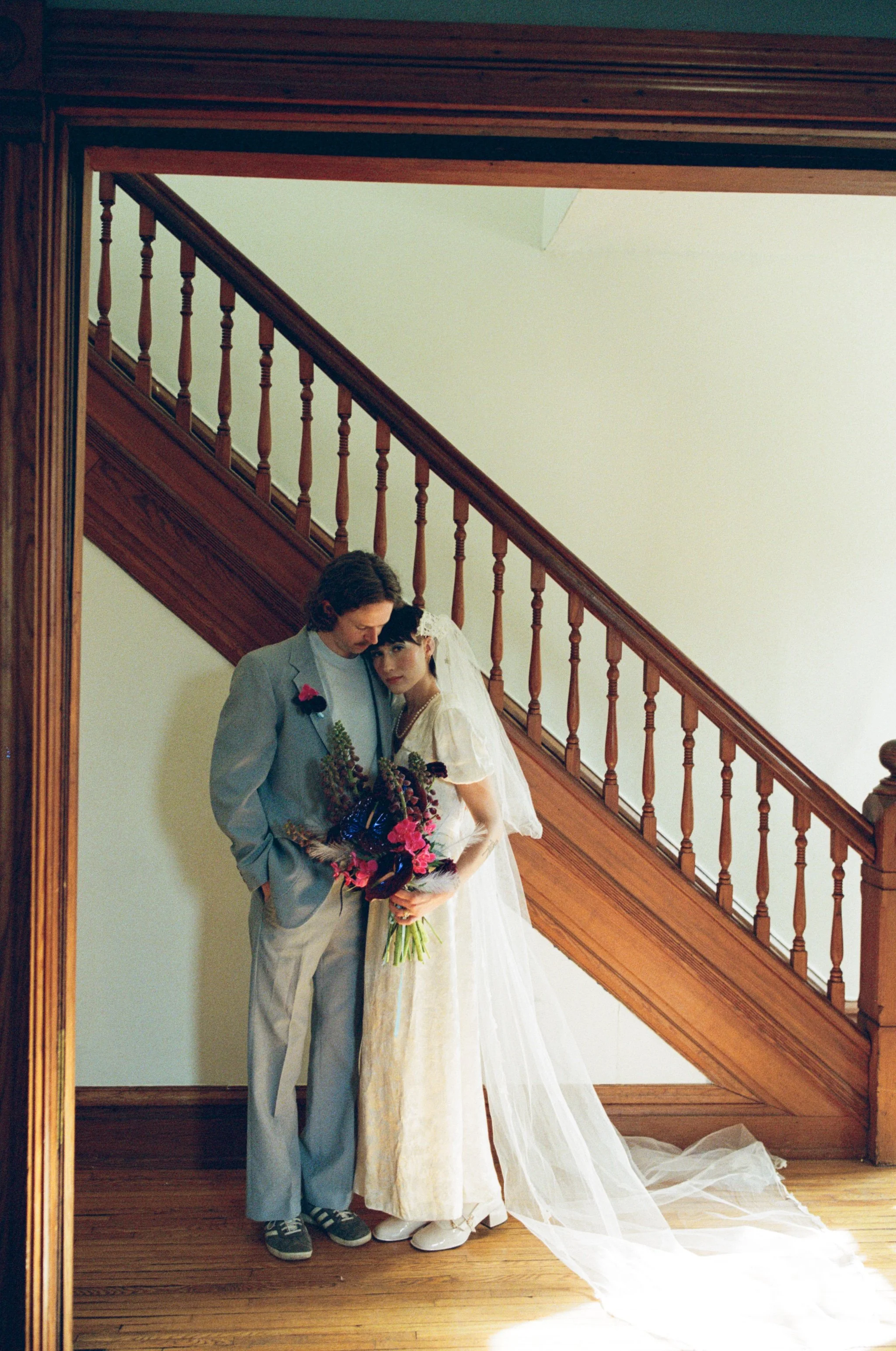 Couple snuggled up together on their wedding day standing in front of a grand staircase in old house