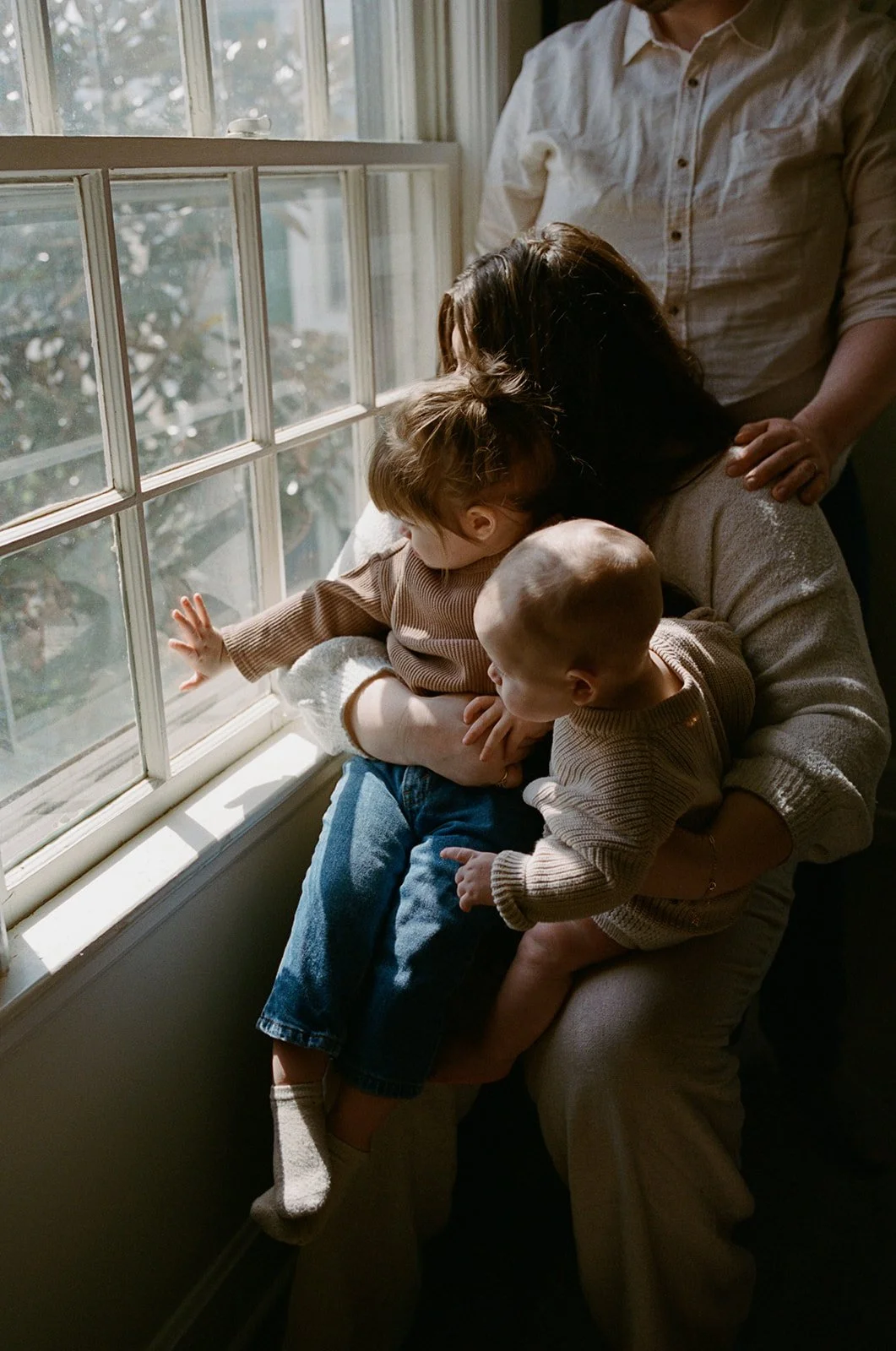 Mom holding two children looking out the window of their home with their spouse standing above