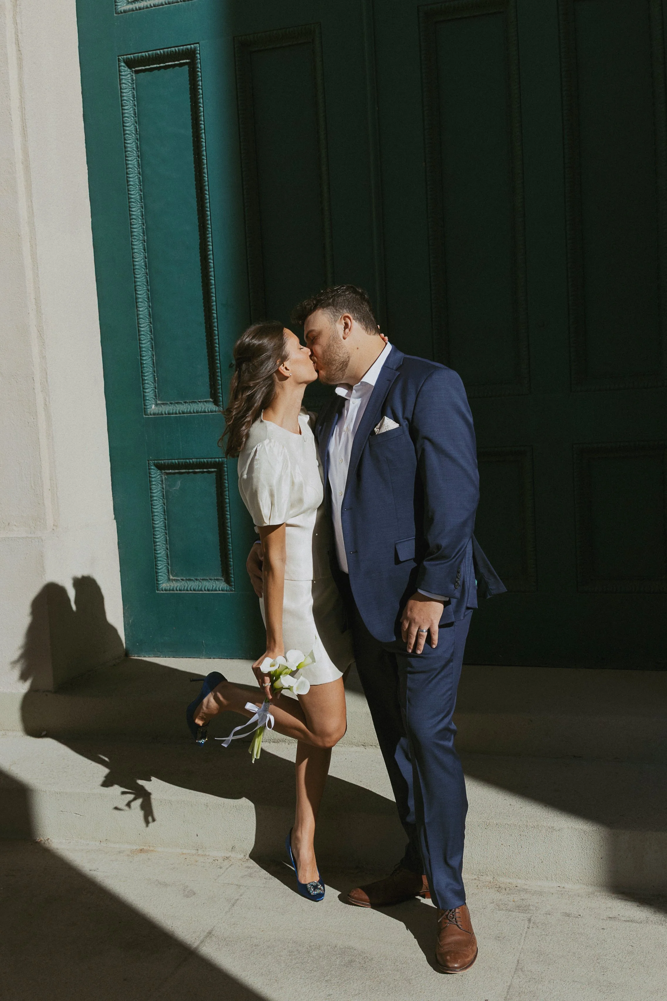 Couple kissing on the steps of a building on their wedding day holding her boutqet