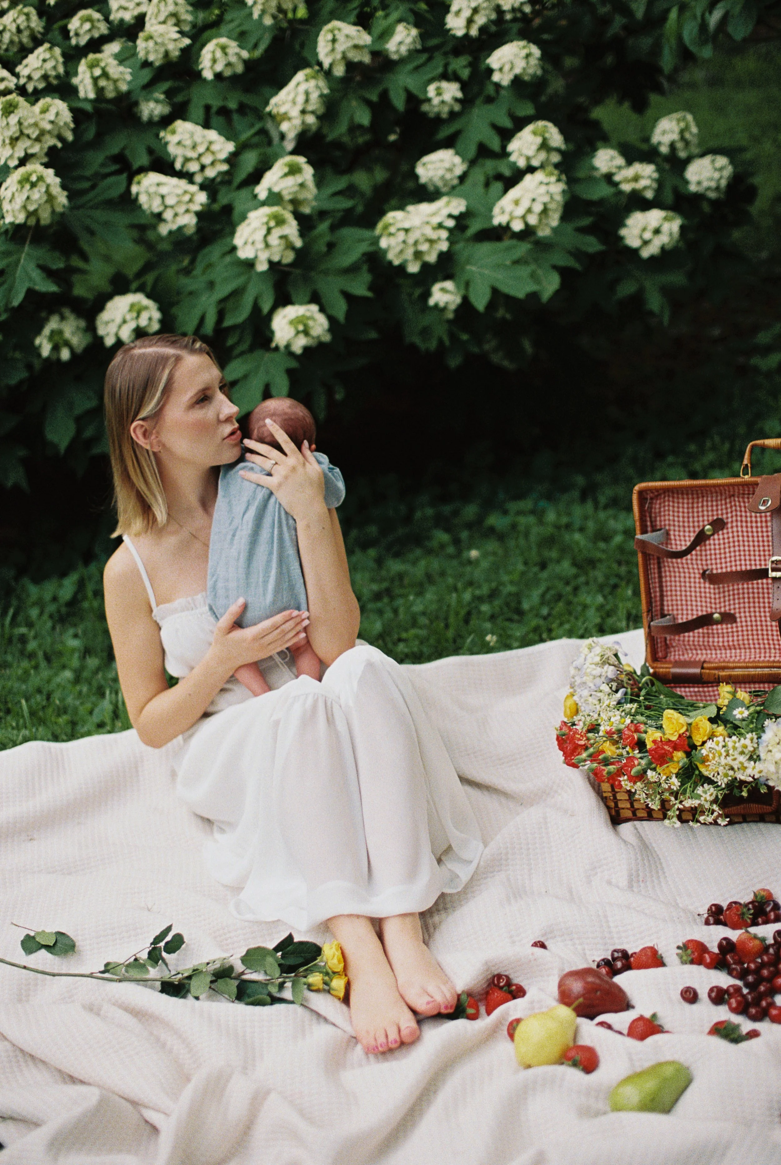 Whimsical shot of a mother holding her baby upon a tablecloth with beautiful flowers blooming in the background
