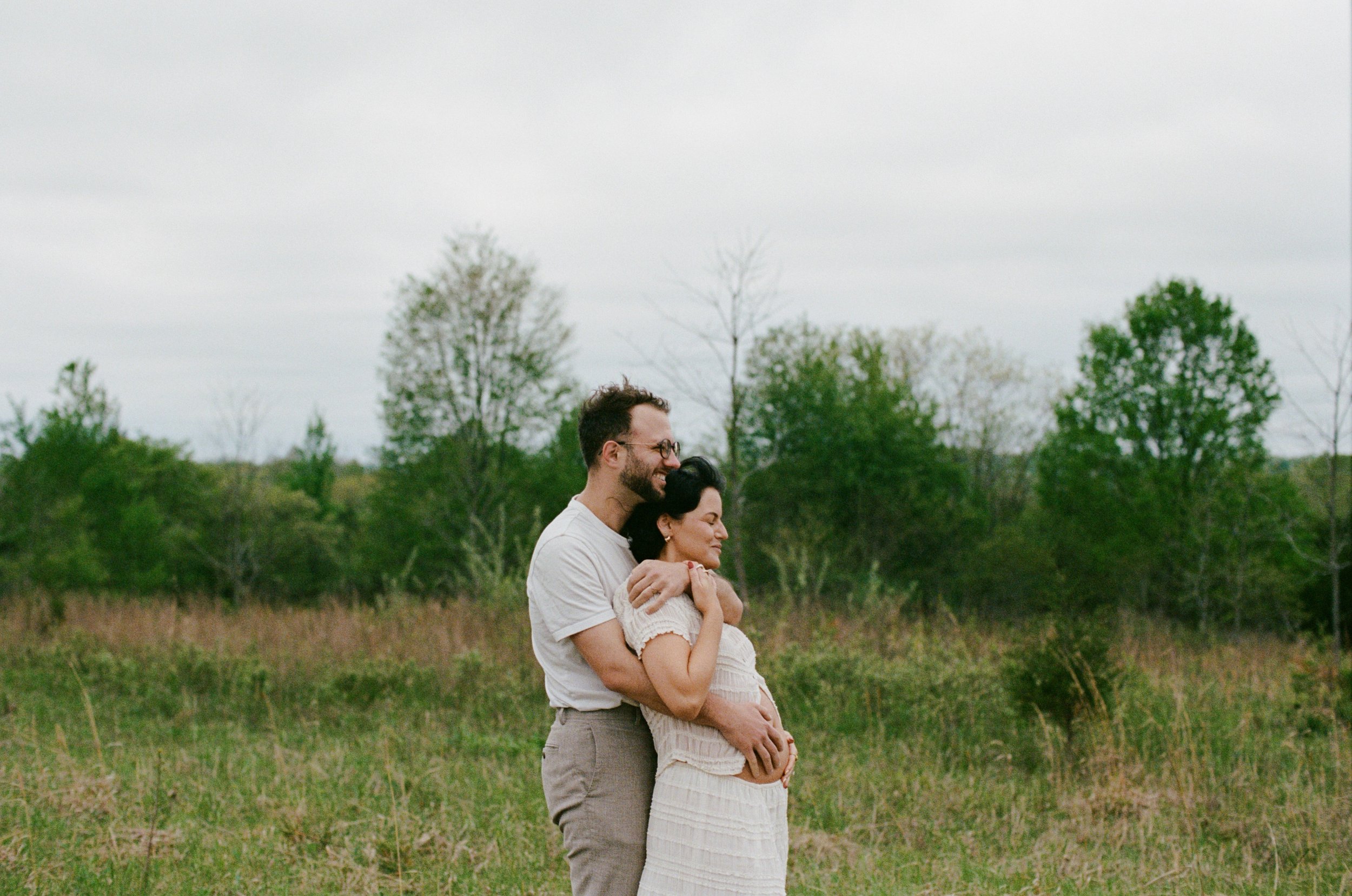 Dreamy photo of a couple standing in a field showing off their growing baby bump