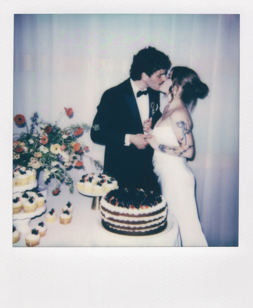 Polaroid of a couple kissing standing next to their wedding cake