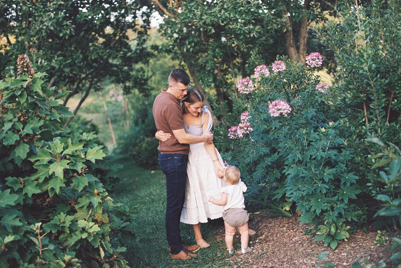 Couple standing in a garden with their young child at their feet looking up