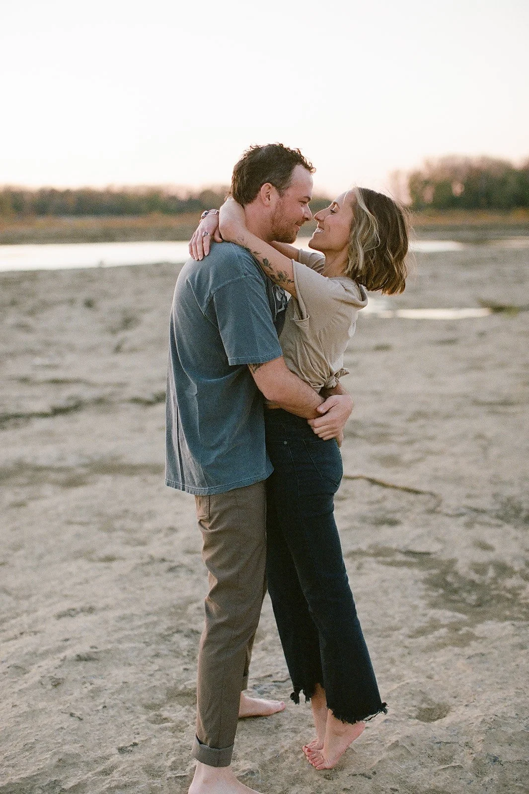 Shot of a couple on the beach, his arms around her smiling at each other