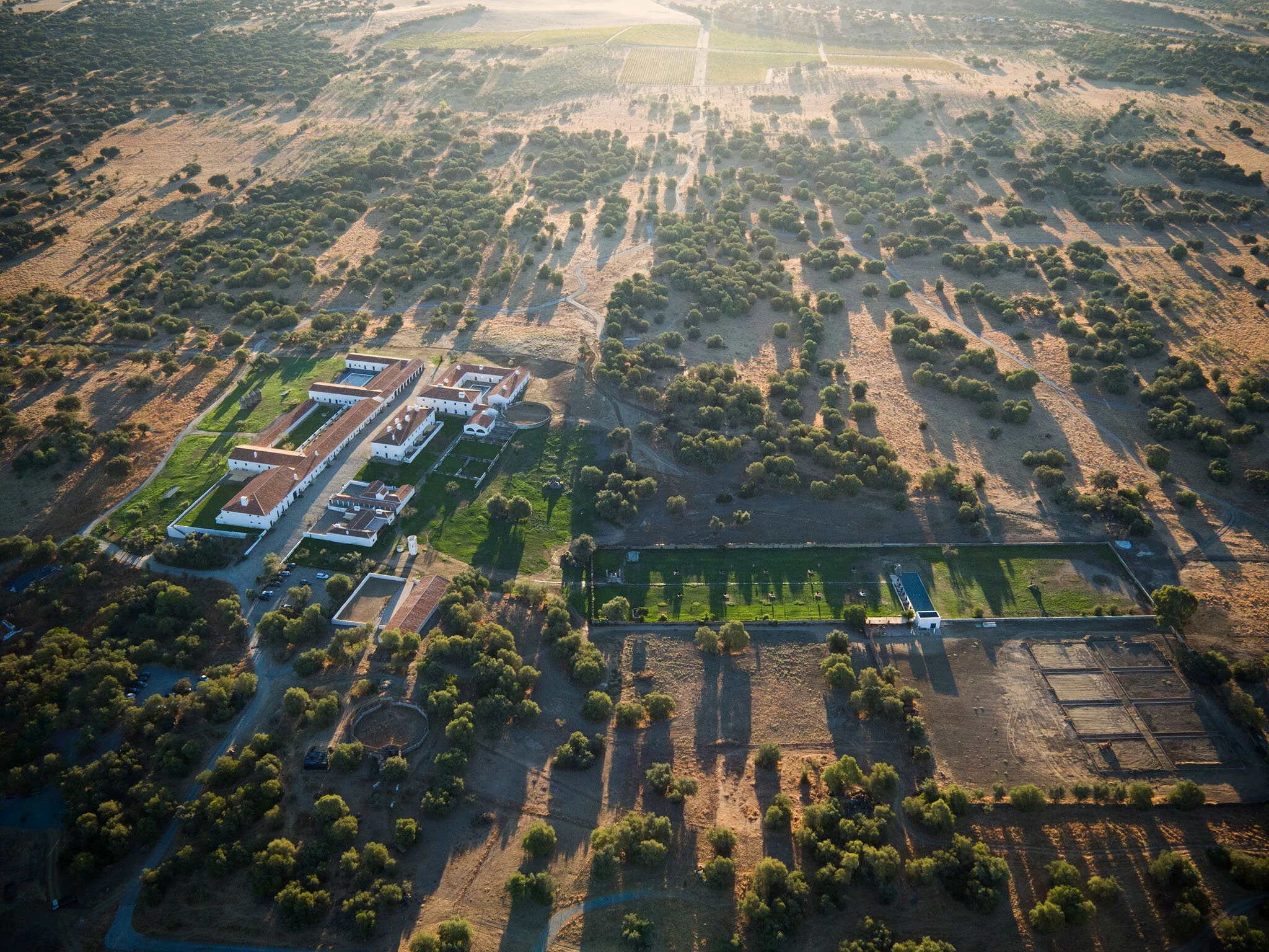 Aerial view of a large estate with multiple white buildings, green lawns, trees, and surrounding farmland and fields.