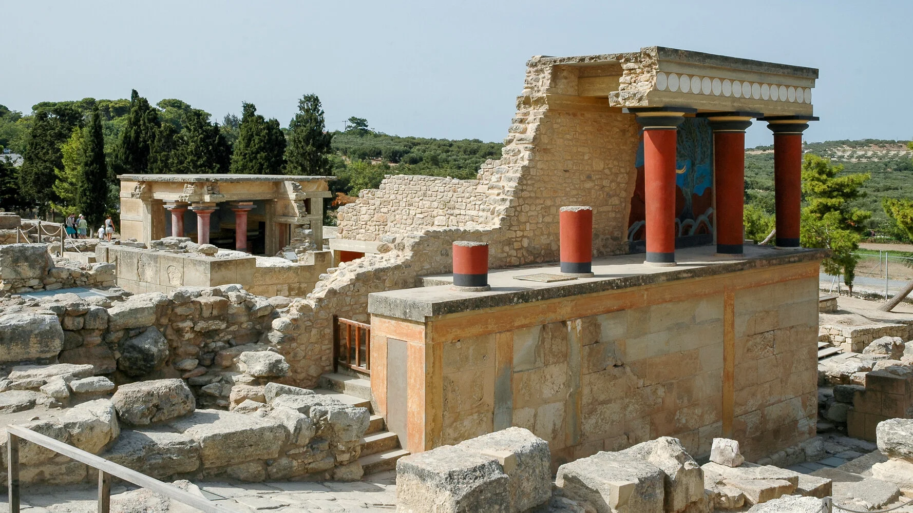Ancient ruins of a stone and stucco building with columns and a mural, possibly part of a historical site or archaeological excavation site.