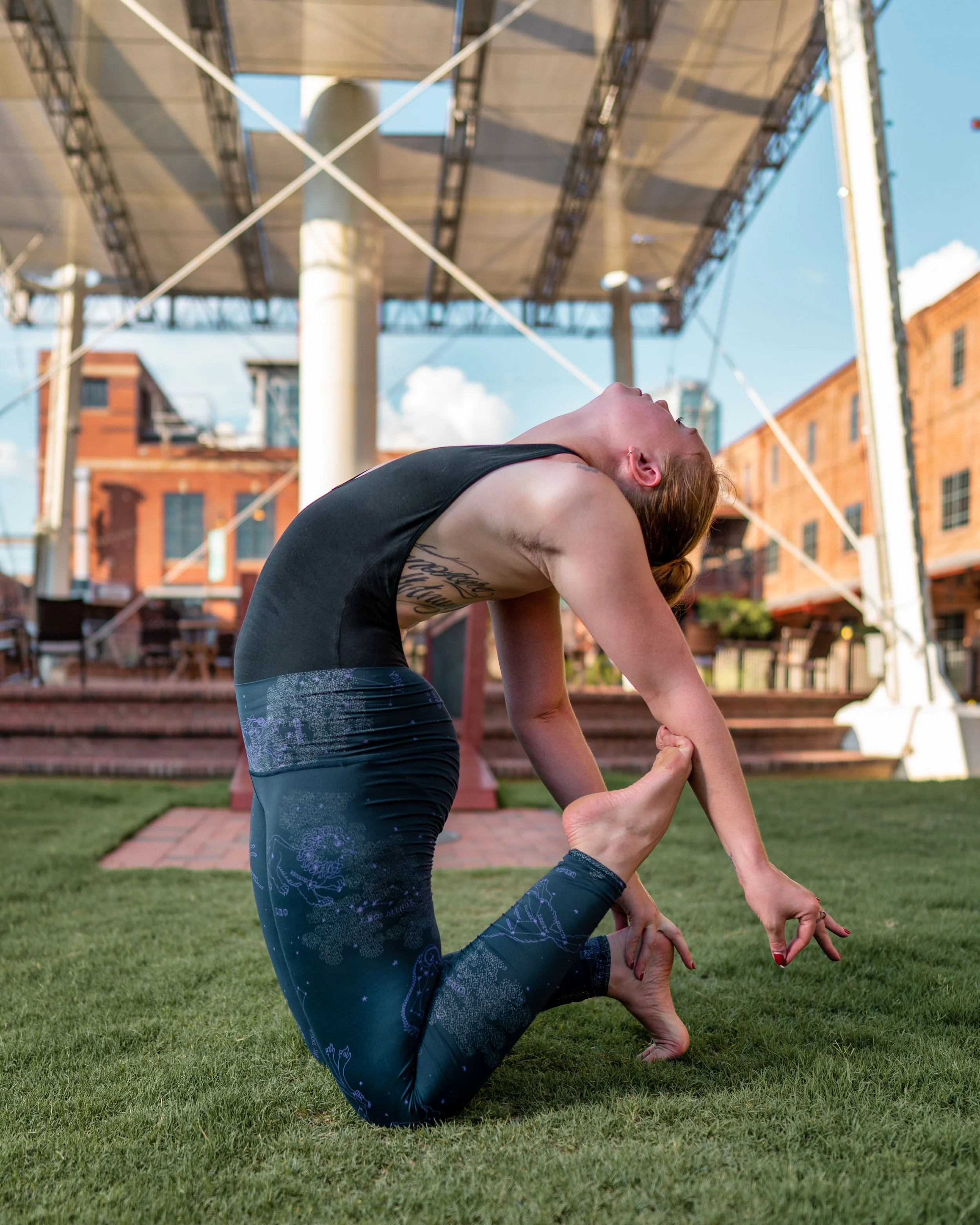 Person doing a yoga camel pose outdoors under a canopy.