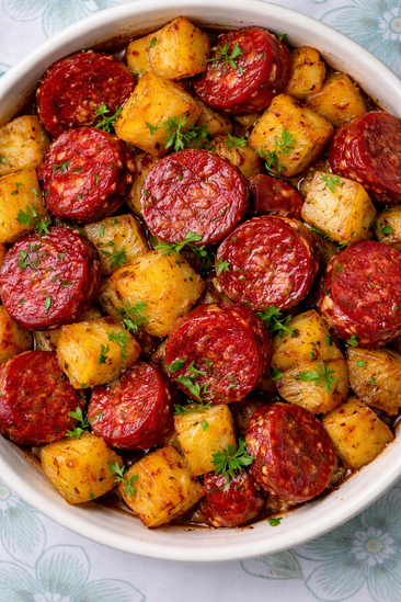 A white bowl filled with cooked sliced sausage and diced potatoes, garnished with parsley.