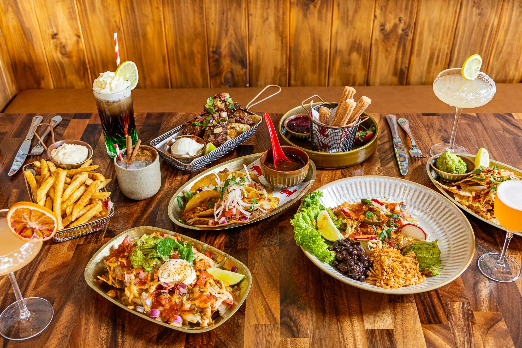 Table spread of Mexican dishes including nachos, Mexican cocktails, churros, tacos, enchiladas