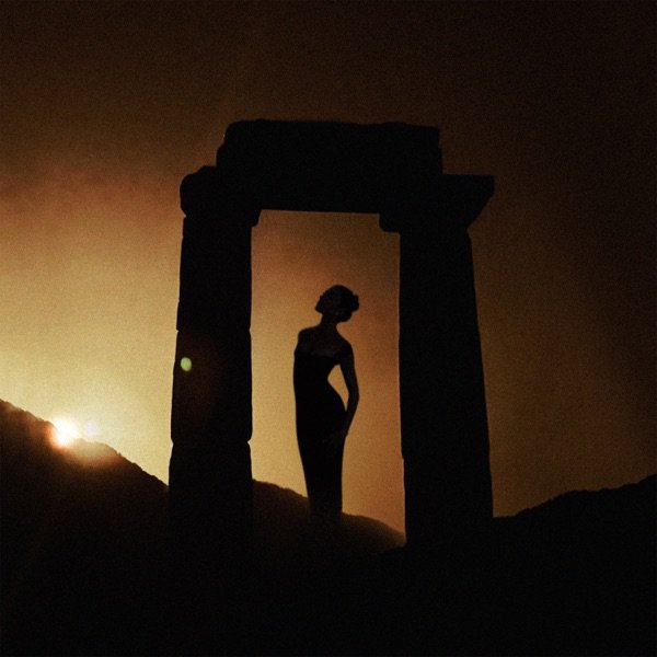 Silhouette of a woman standing in a doorway-like stone structure on a hillside during sunset or sunrise.