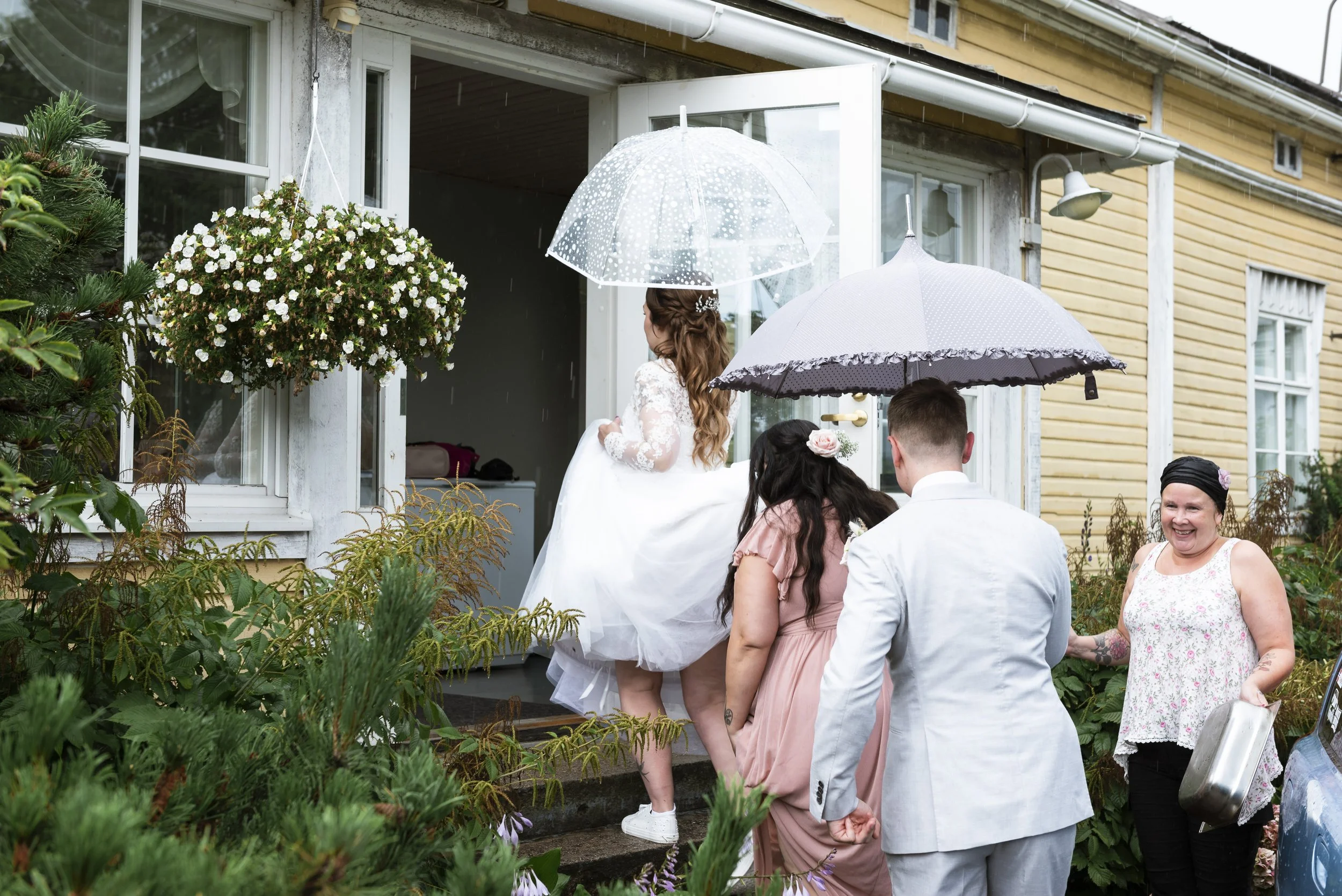 Sateenvarjoja käsissään pitelevät häävieraat kävelet rappusia ylös juhlatilaan.