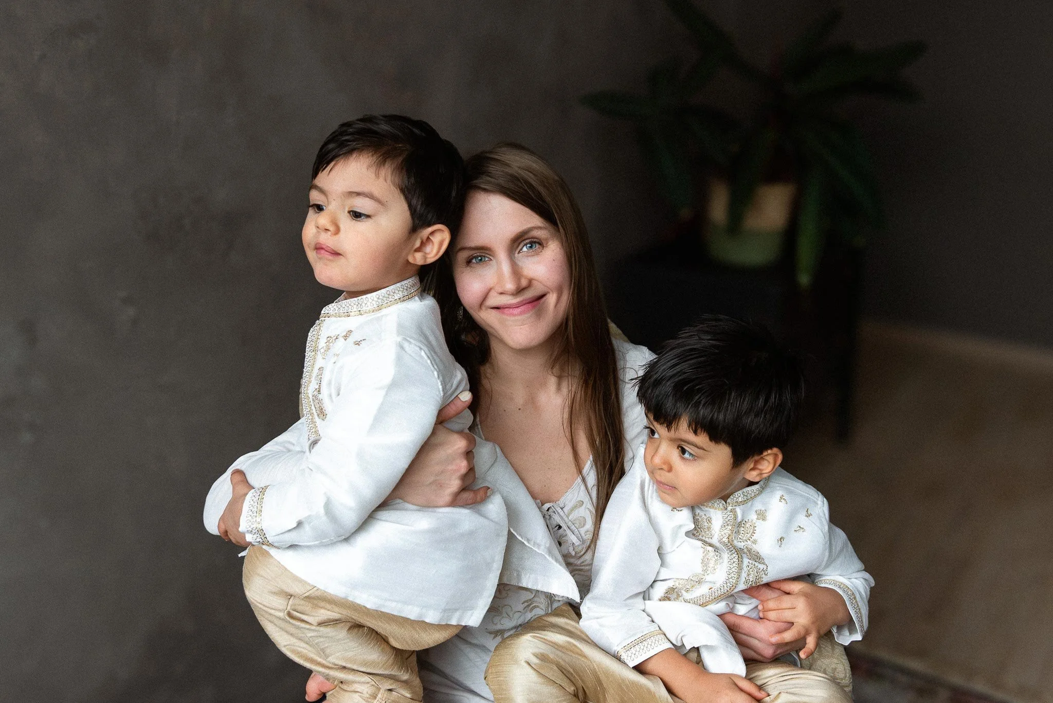 Hymyilevä nainen katsoo kameraan ja pitää sylissään kahta lastaan.