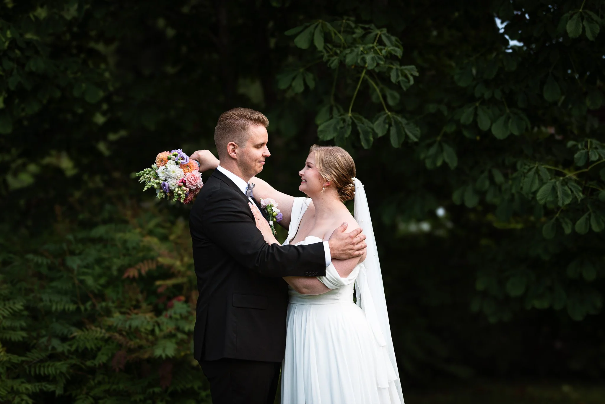 Hääpari katsoo toisiaan hymyillen tummanvihreän luonnon keskellä.