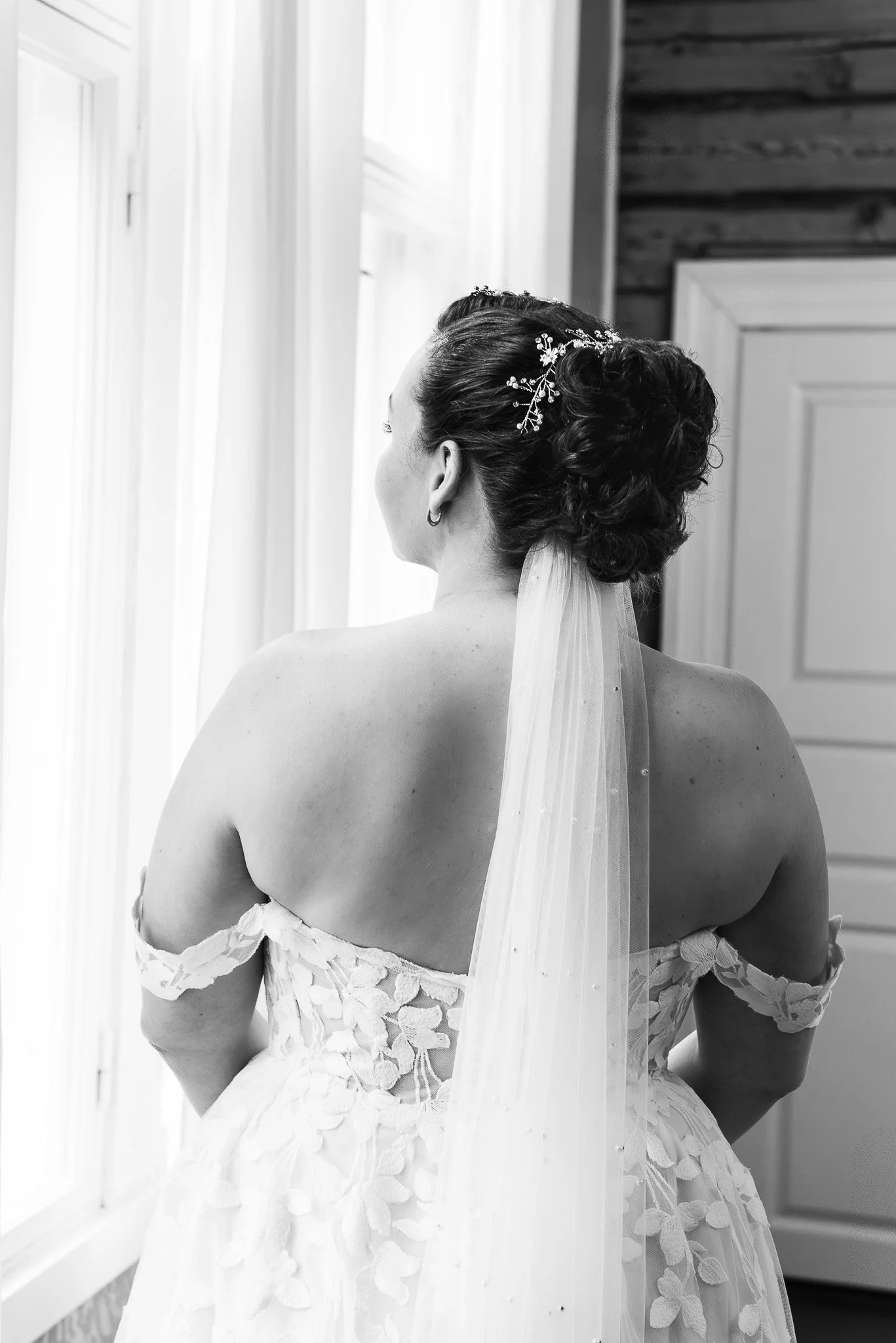 Morsian seisoo selkä kohti kameraa, hänen tummat hiuksensa ovat nutturalla ja selkää pitkin on huntu.