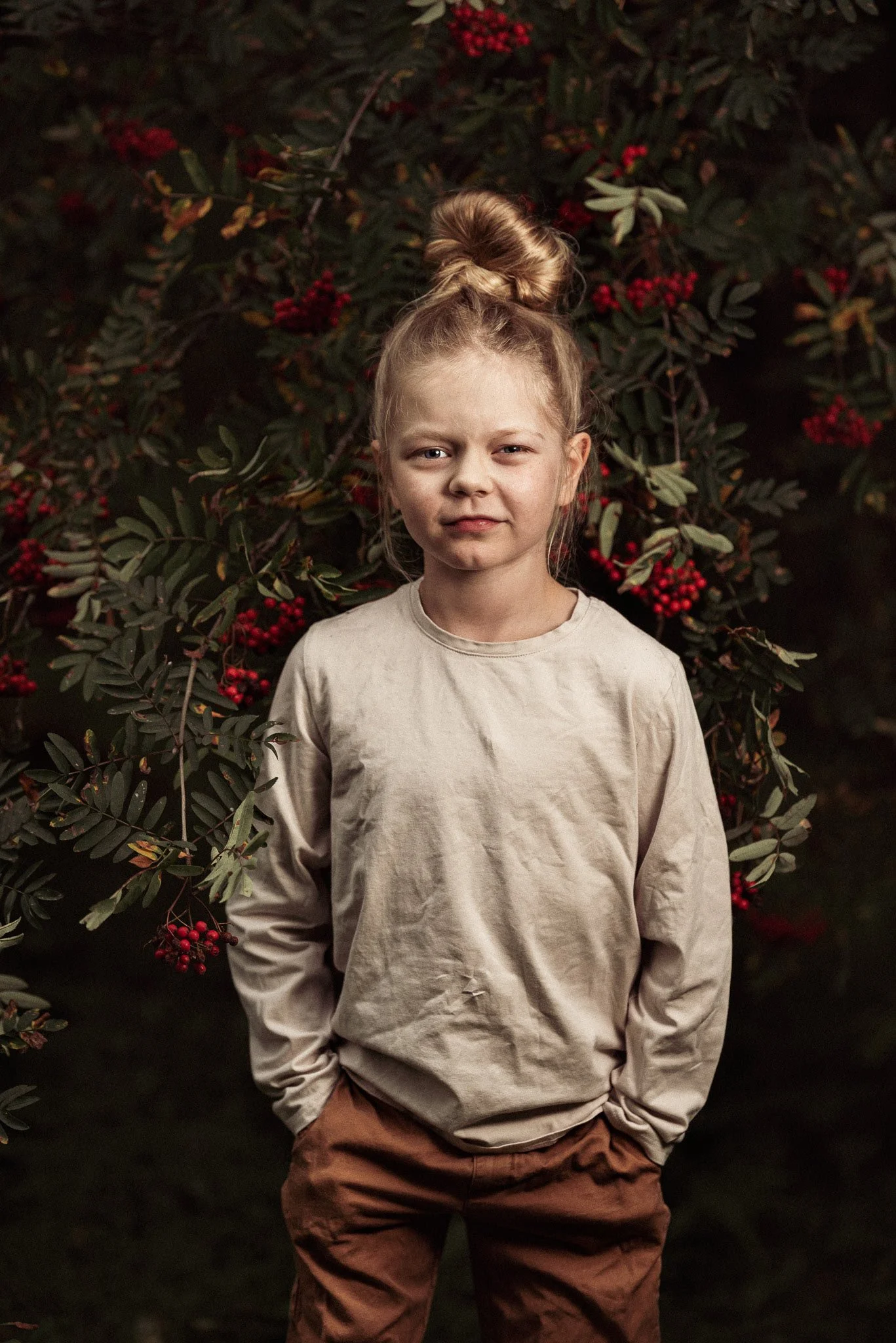 Lapsi seisoo marjoja täynnä olevien pihlajanoksien edessä ja katsoo kameraan.