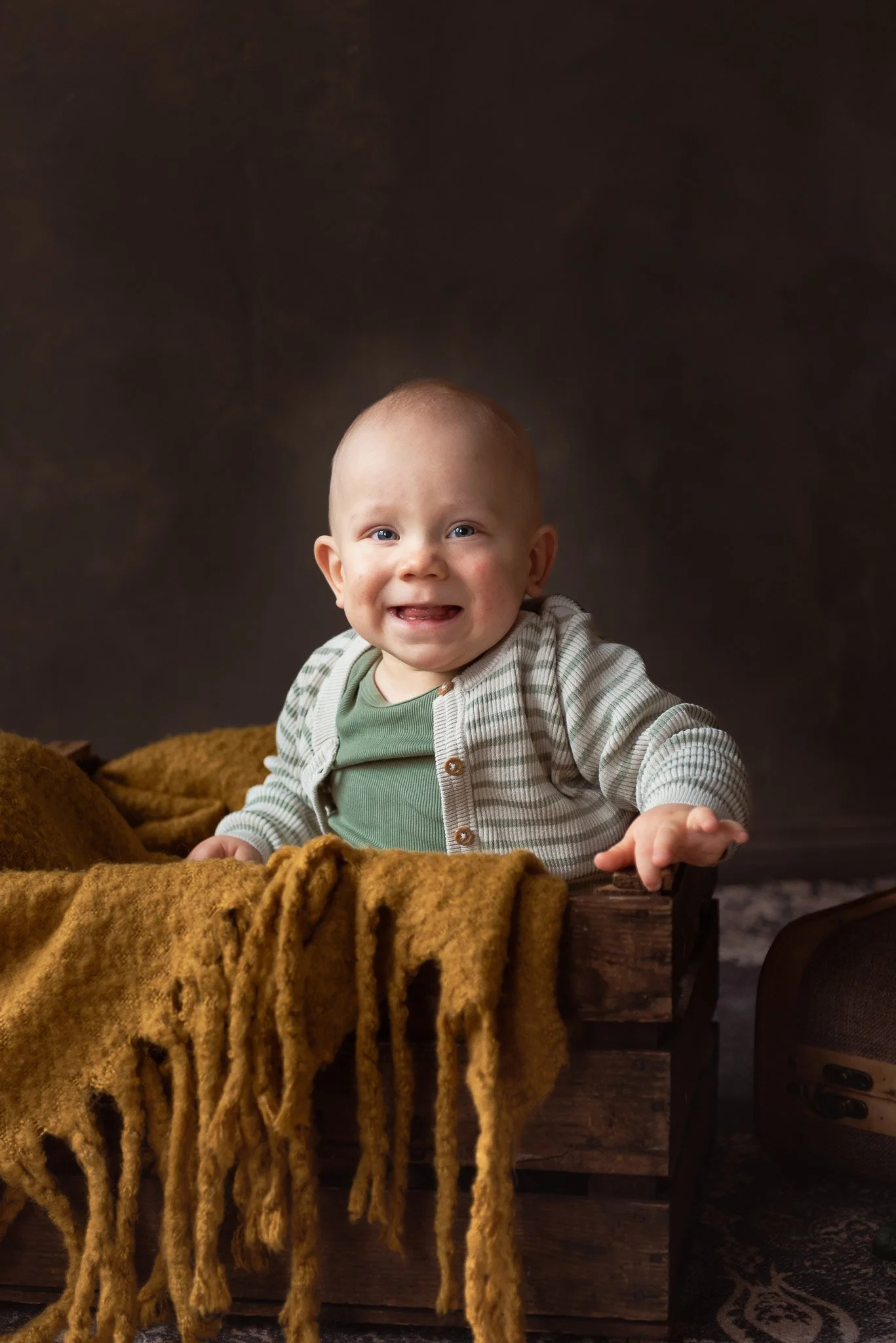 Leveästi hymyilevä vauva istuu puulaatikossa ja katsoo kohti kameraa.