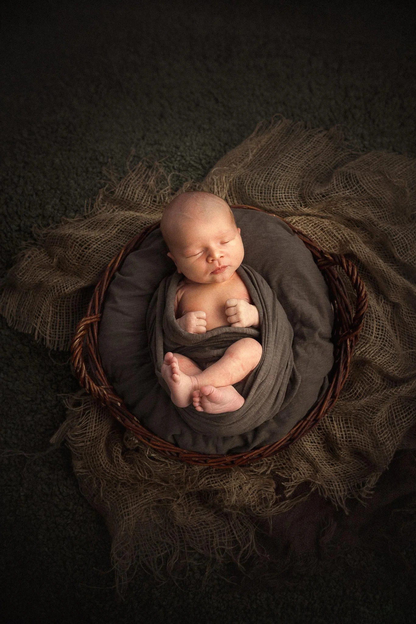 Ruskeansävyisiin kankaisiin kääritty vauva nukkuu korissa.