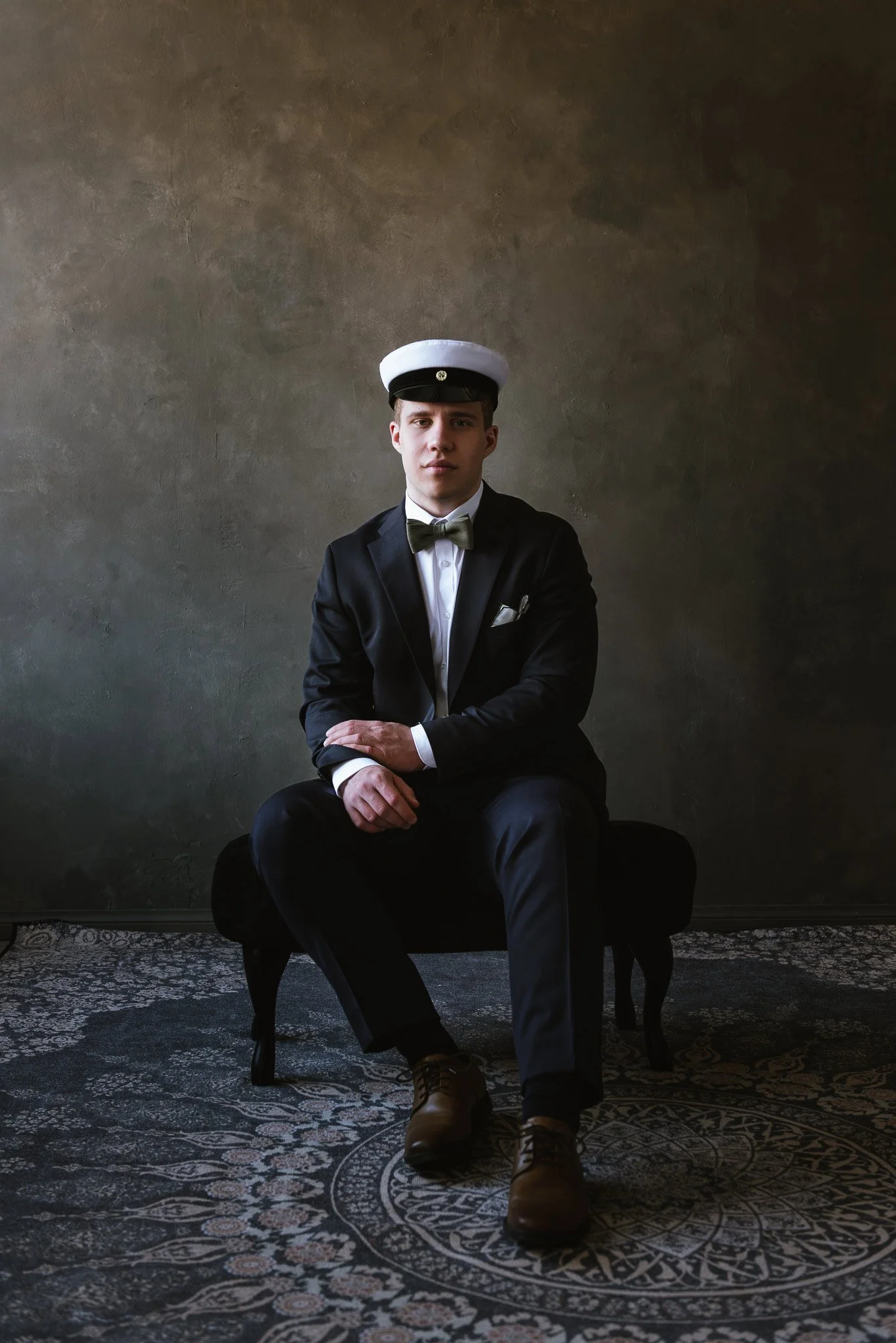 Nuori mies istuu puku päällä ja ylioppilaslakki päässä ja katsoo kameraan.