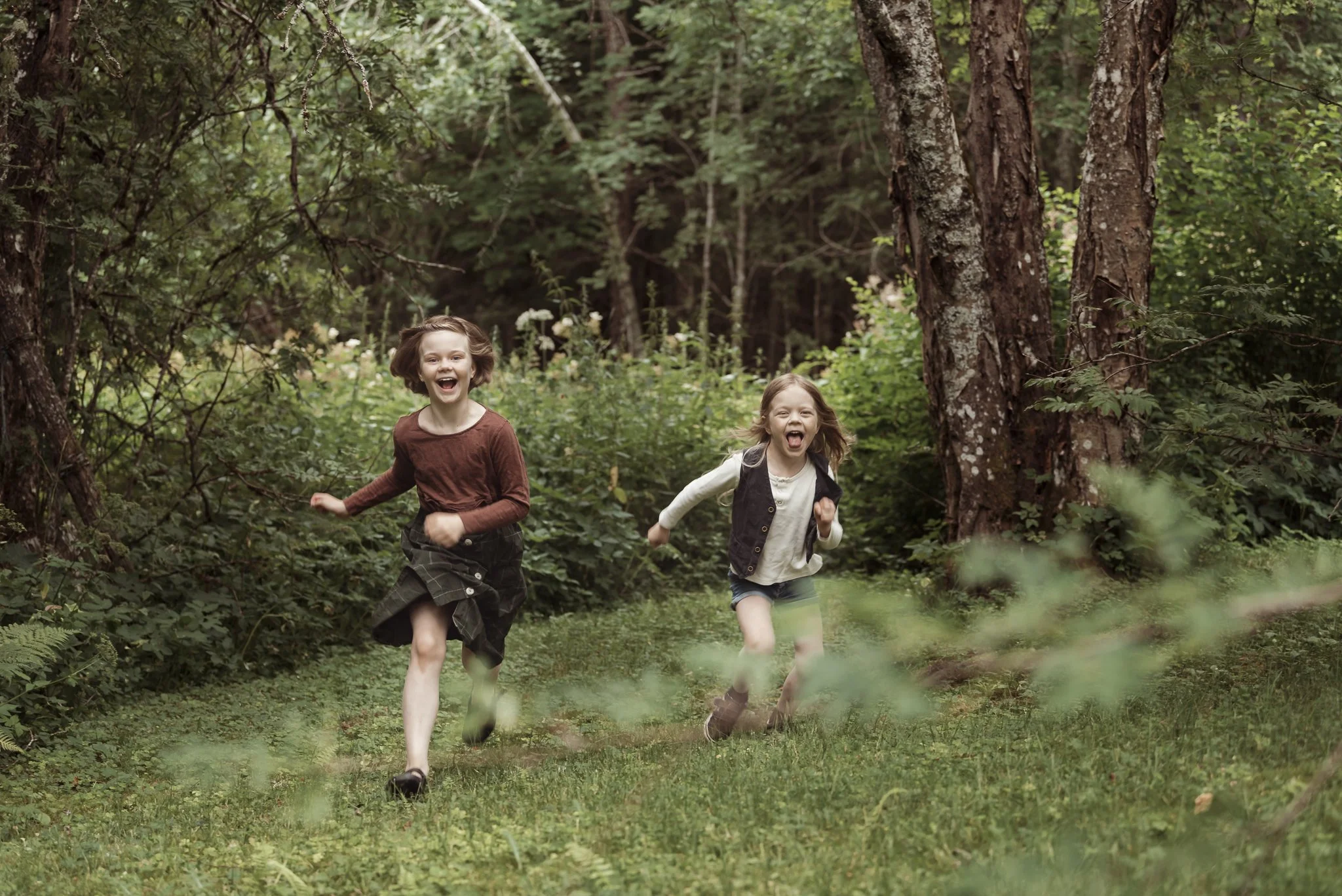 Kaksi lasta juoksee nauraen metsässä.