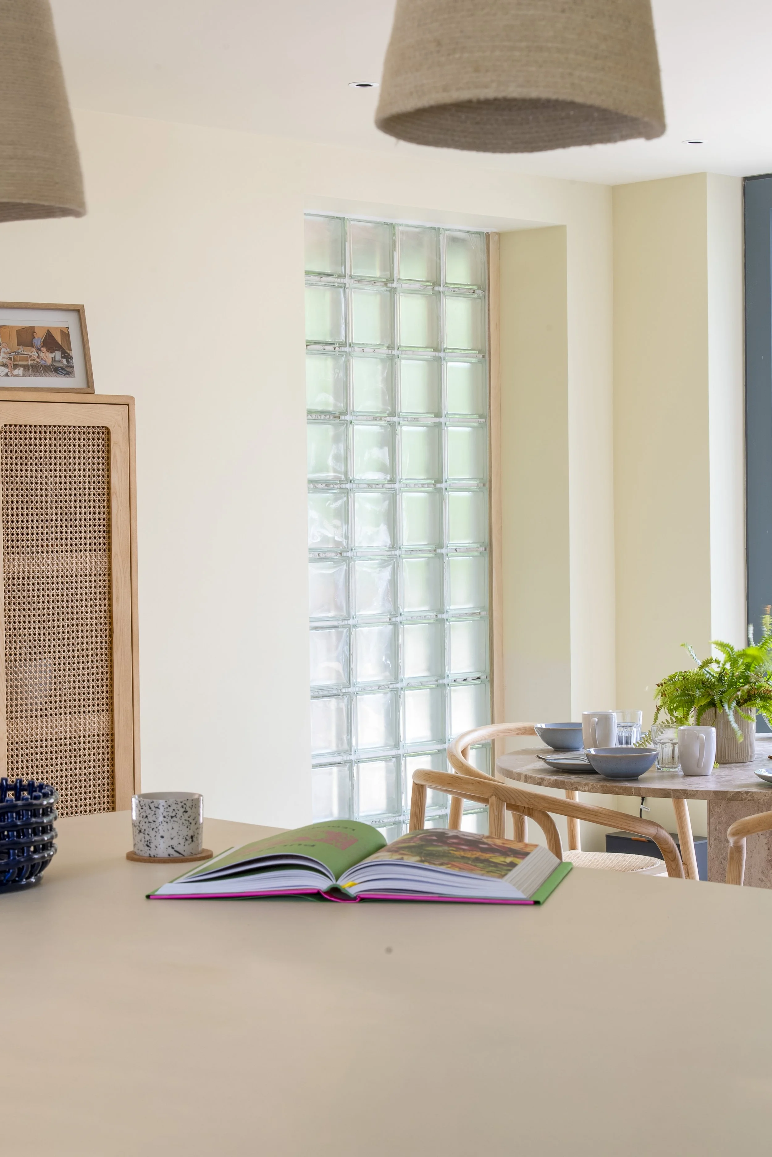A quiet dining space defined by soft tones, natural materials, and diffused light. Glass block detailing introduces privacy while maintaining brightness, complemented by warm timber furniture and subtle textural contrasts that create a relaxed, lived