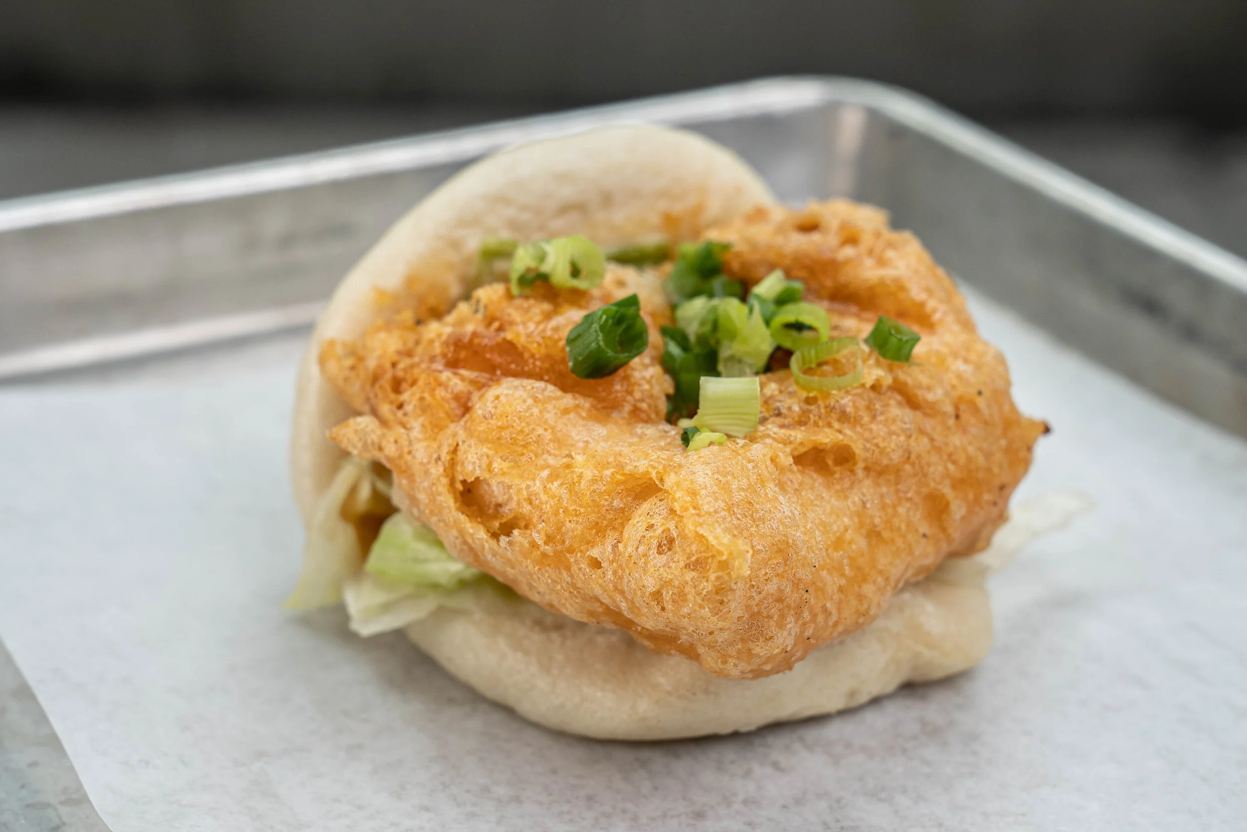 SRIRACHA TOFU BAO - Fried tofu with bao sauce, sweet soy glaze, lettuce, and green onions.