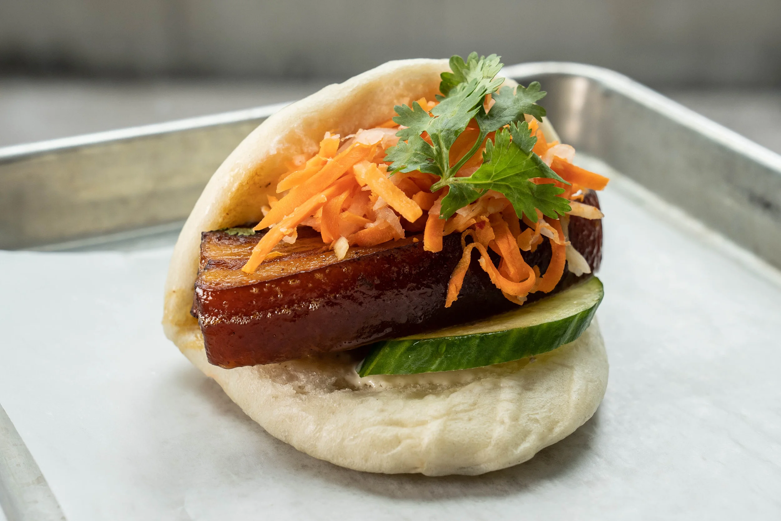 FIVE SPICE BELLY BAO - Braised pork belly in our five spice sauce, with garlic mayo, cucumbers, pickled daikon and carrots, and cilantro.