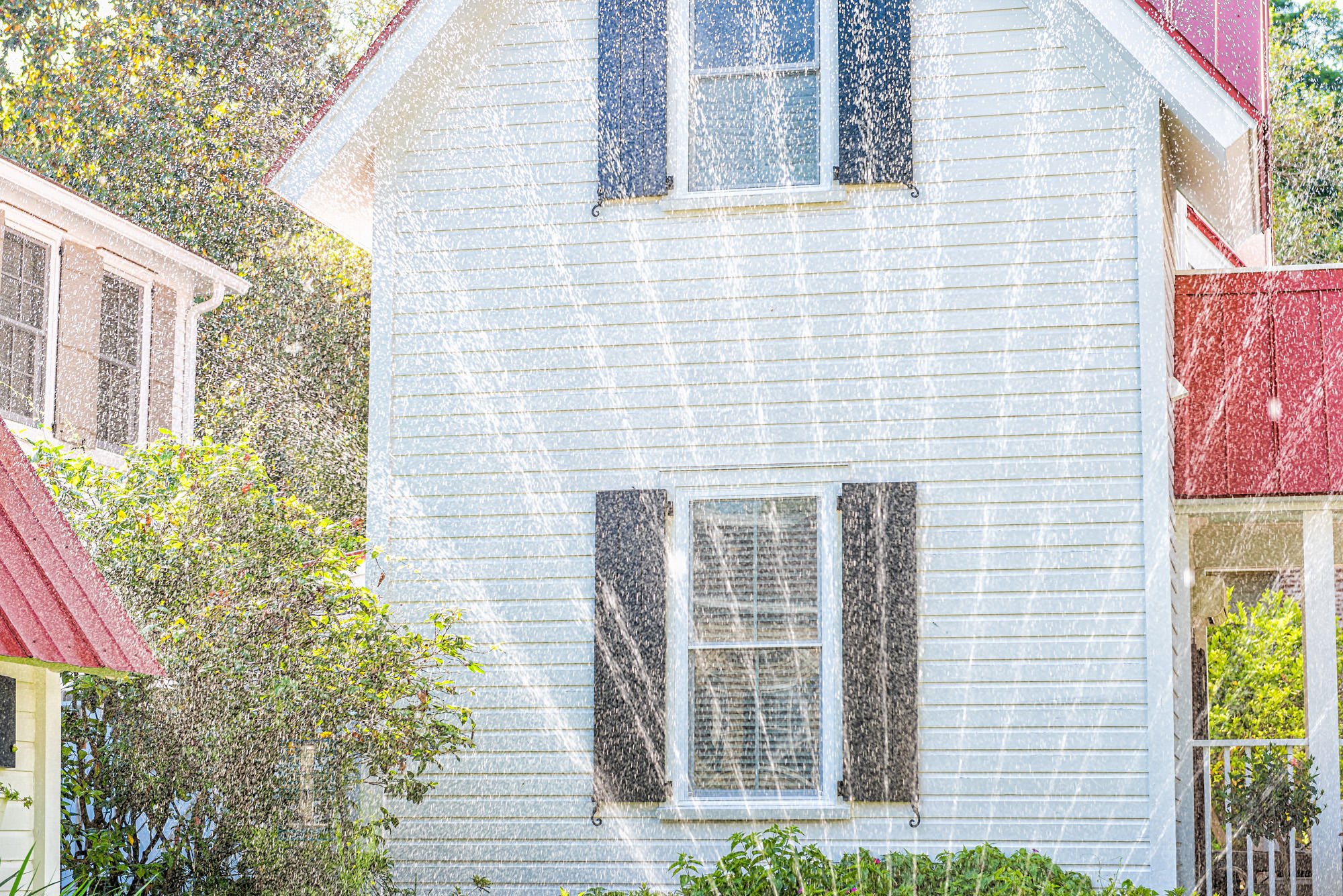white home with red roof with sprinkler in yard - curb appeal ideas