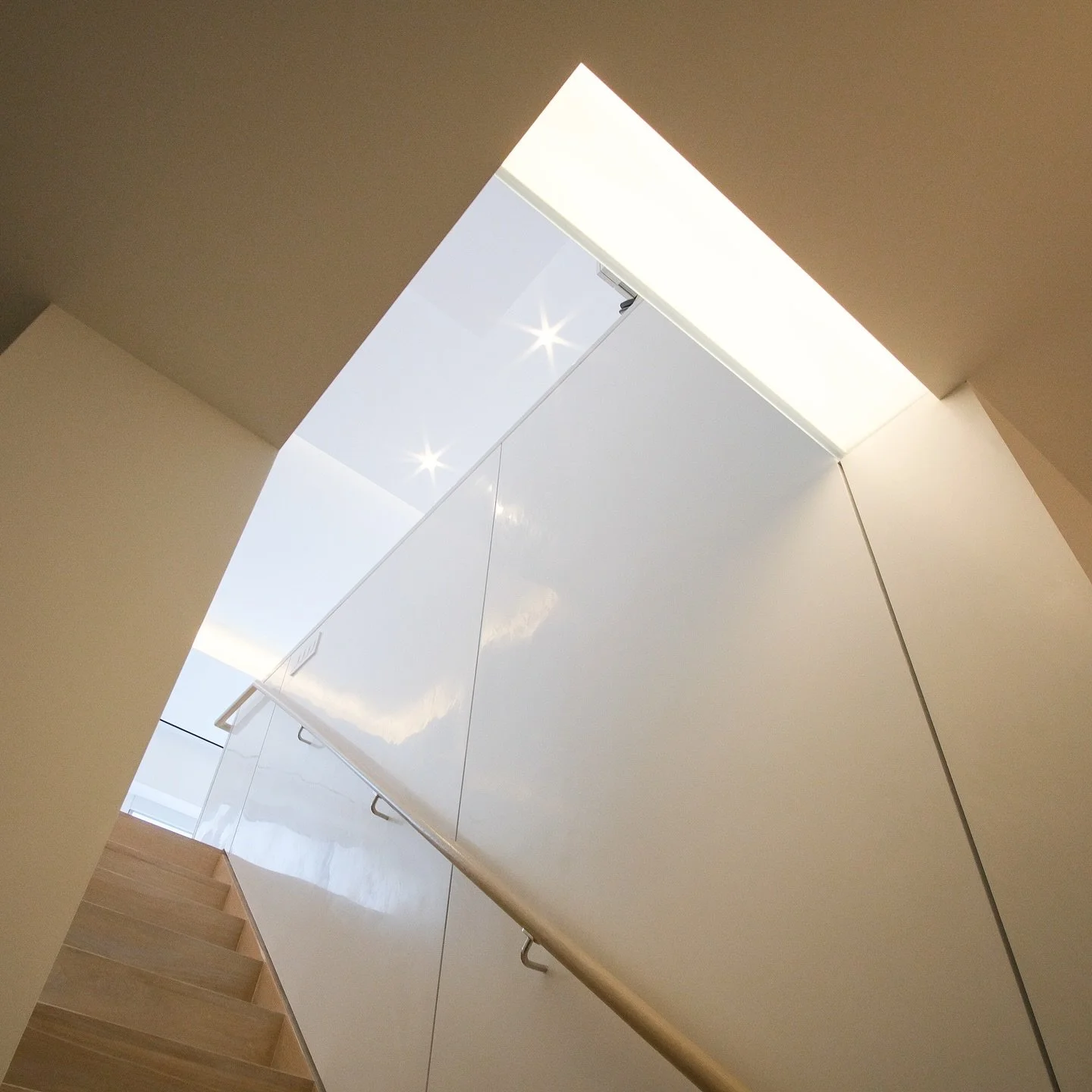 Staircase detail from our gut renovation of a duplex at Worldwide Plaza. The stair features stained solid white oak treads, a custom-crafted white oak handrail with concealed hardware, and a white polished plaster wall. Above, a backlit glass ceiling