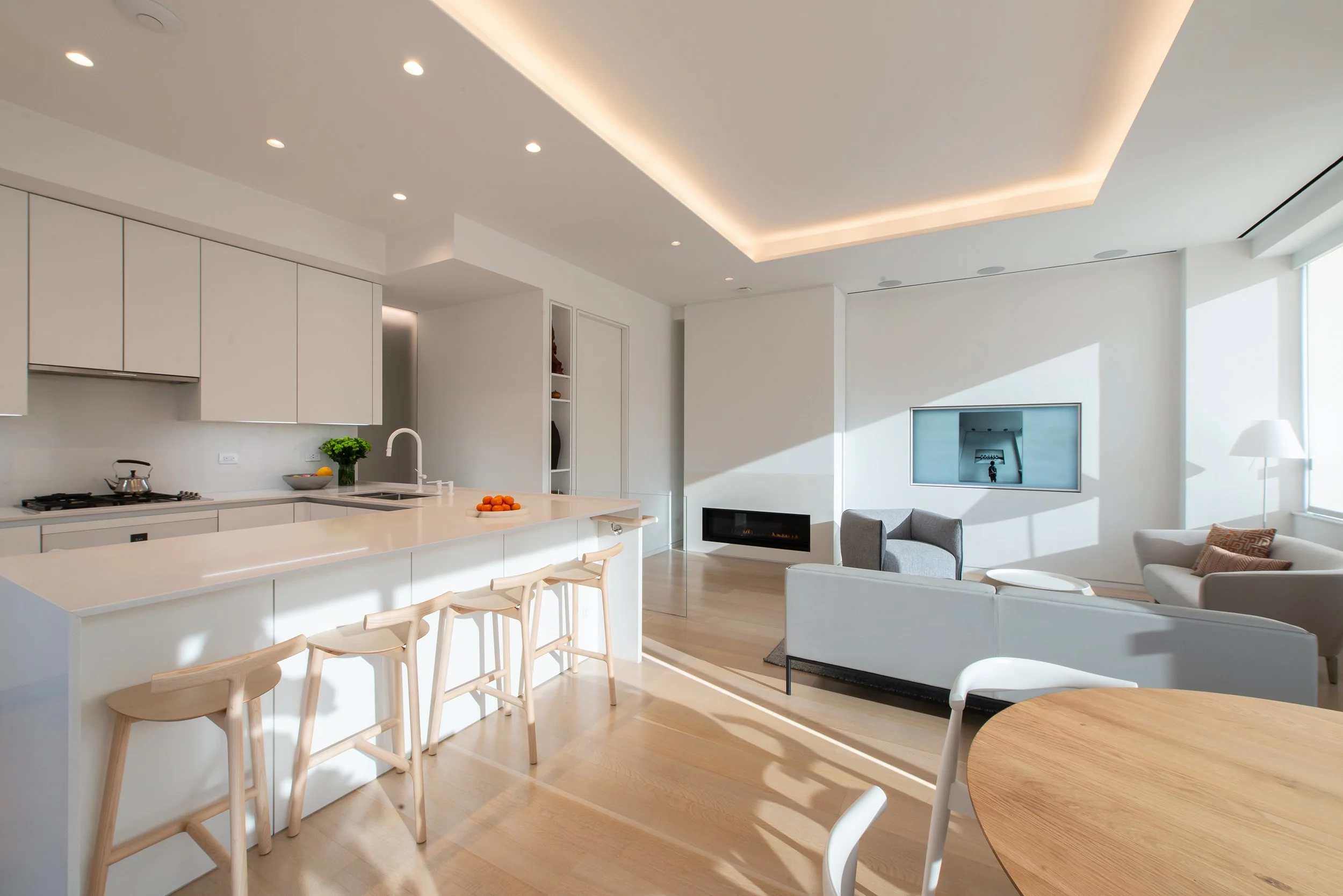 Contemporary open living space with kitchen, dining, and living room functions unified by a large light cove. The all-white color of the kitchen belies its durability as it's finished in highly durable stain resistant materials. 