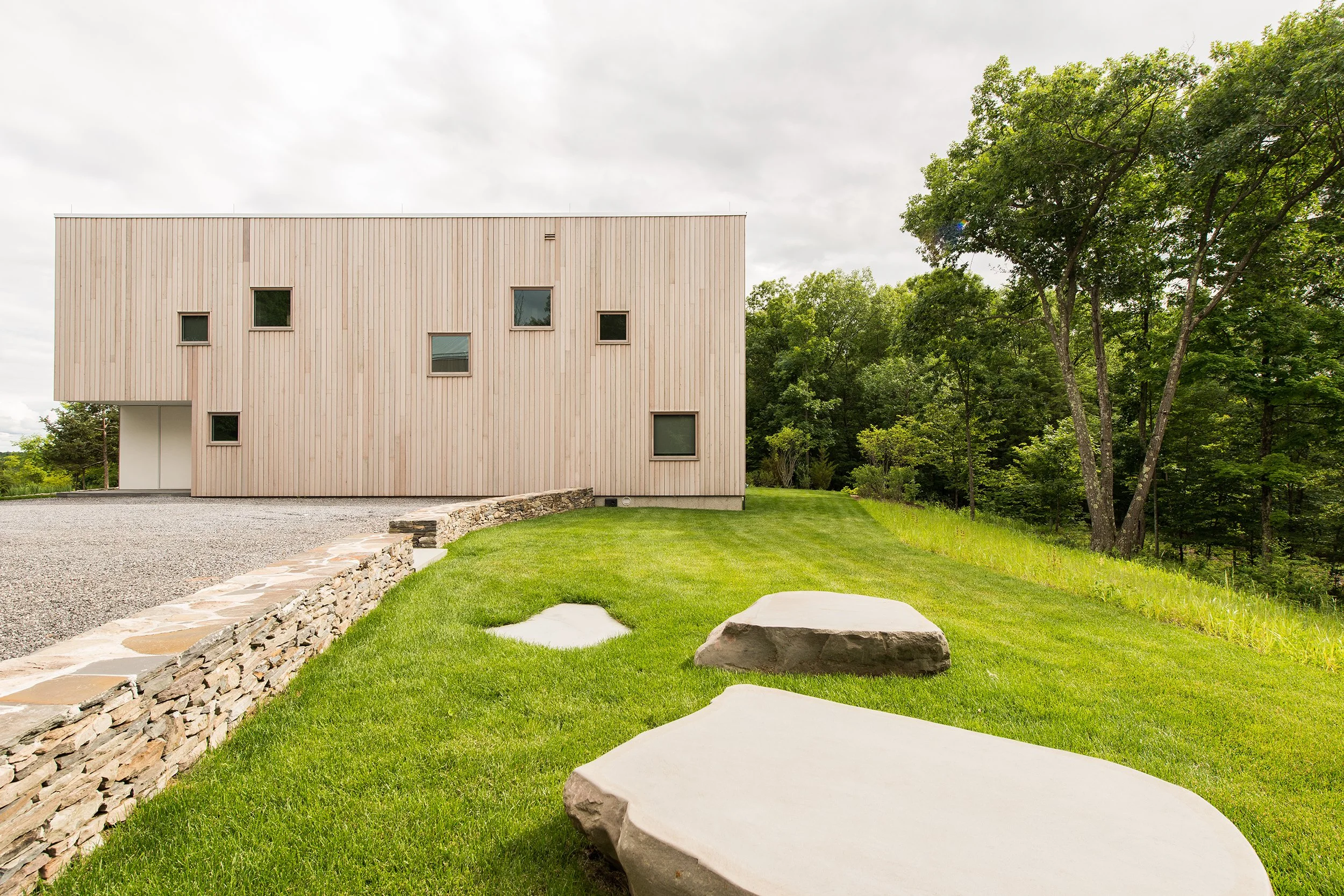 Contemporary house in the Hudson River Valley. Stained custom-profile vertical cedar cladding with large hardwood windows. Large cut and polished boulders serve as seating towards the mountainous vistas and aligned for sunset views.