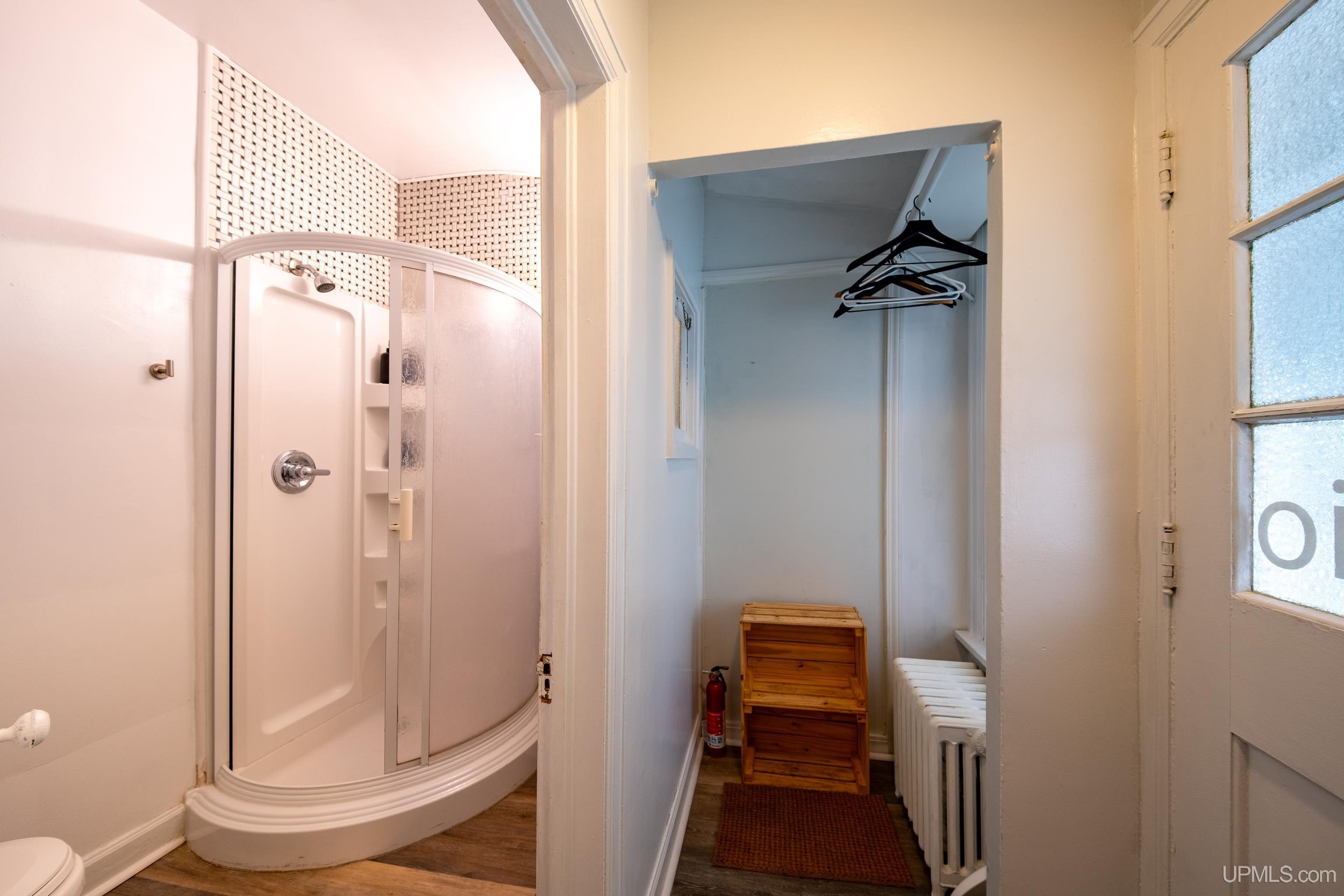 Standing shower inside a white bathroom with a closet to the right.