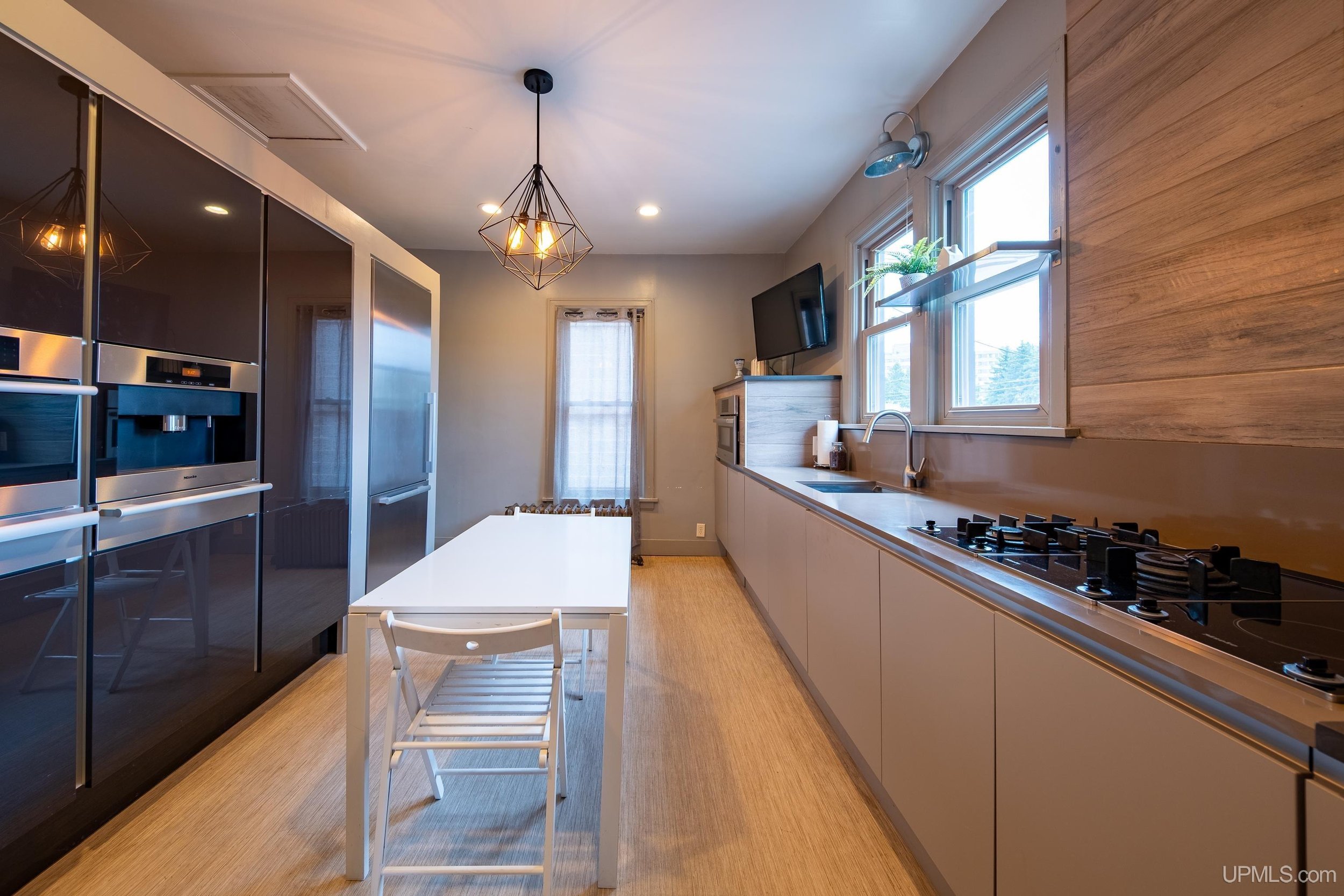 A kitchen with gas burners, ovens on the opposing wall, and a white table and chairs in the center of the room.