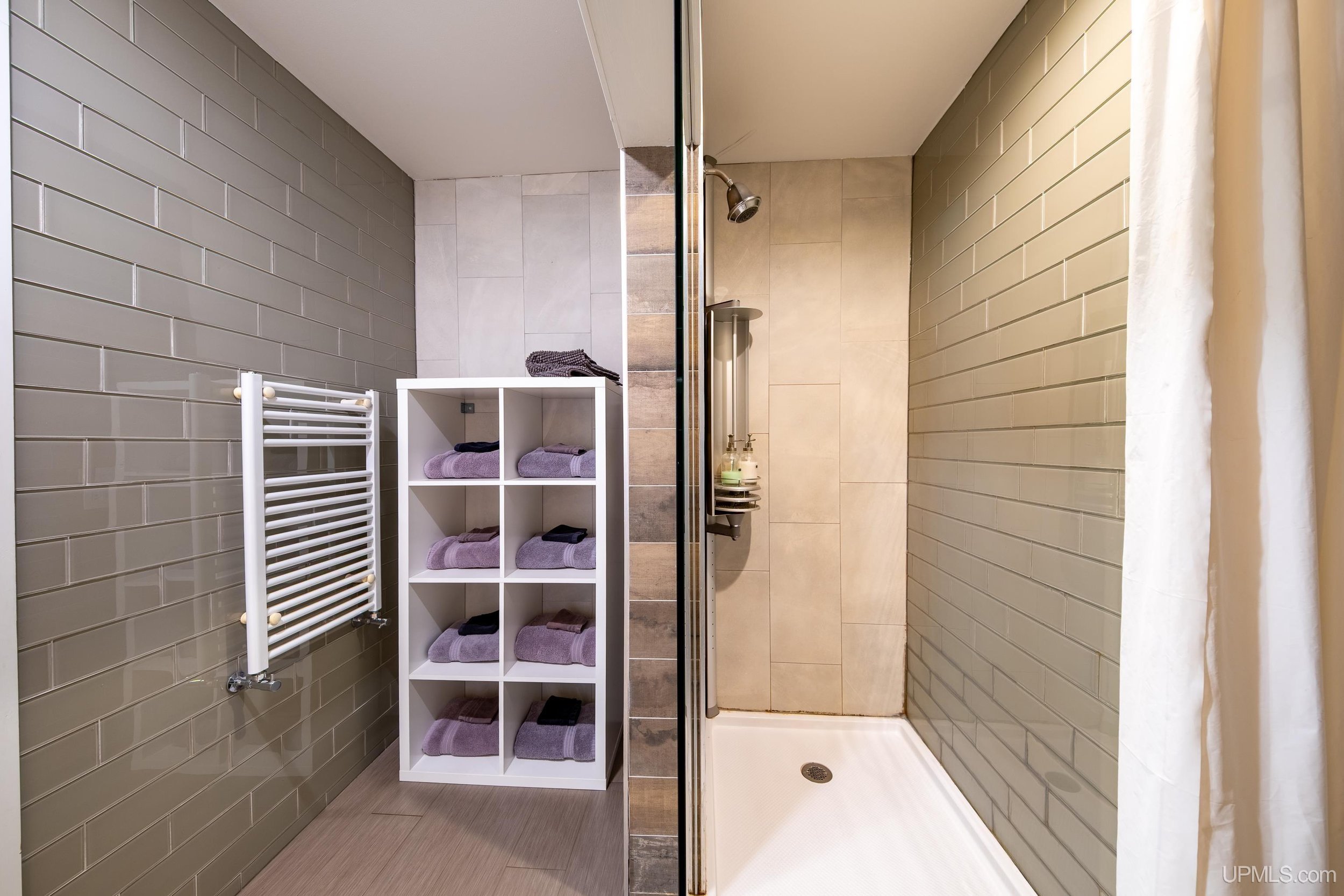Grey tiled bathroom with standing shower and white shelving.
