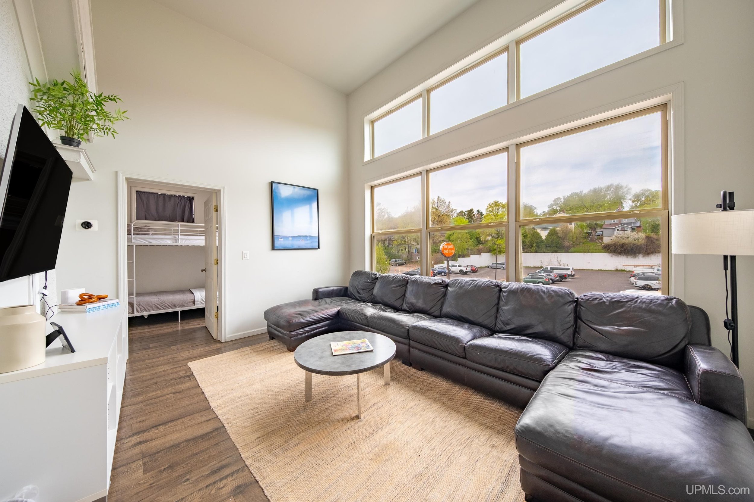 A living area with a couch against the windows, facing towards a mounted TV.