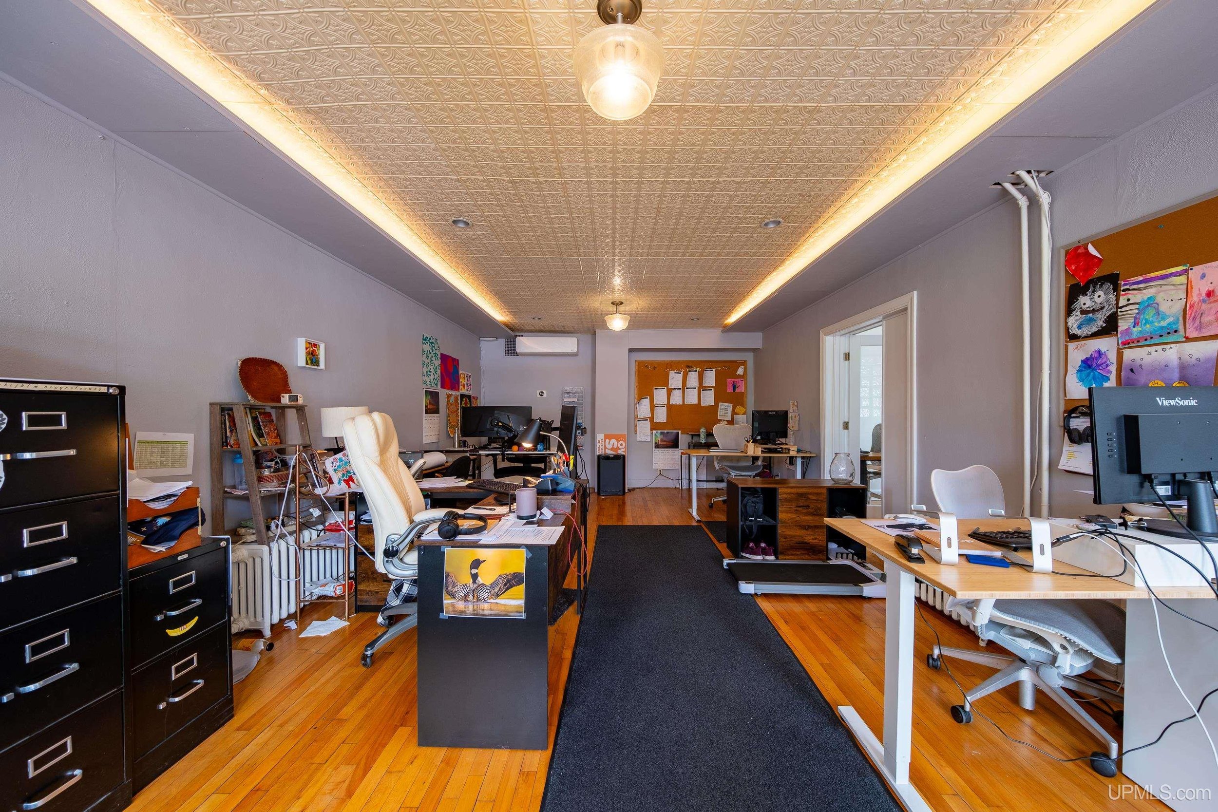An office space with multiple desks, file cabinets, and a bulletin boards.