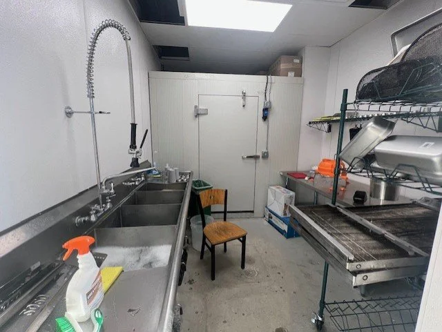 A kitchen area with triple sink and walk in cooler.