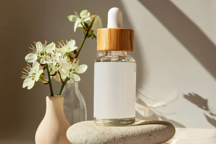 bottle of essential oil on rock with vase of flowers