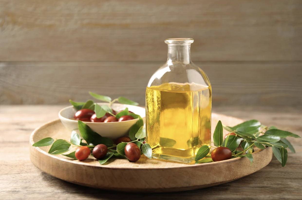jojoba oil in glass bottle with jojoba seeds on wooden table