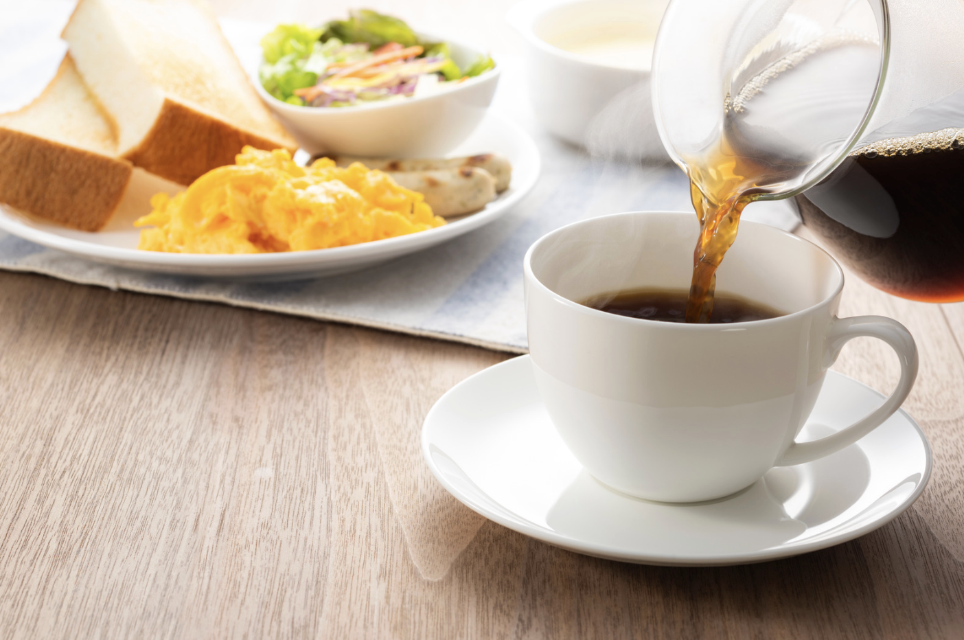 coffee being poured into white cup with plate of eggs and greens in background