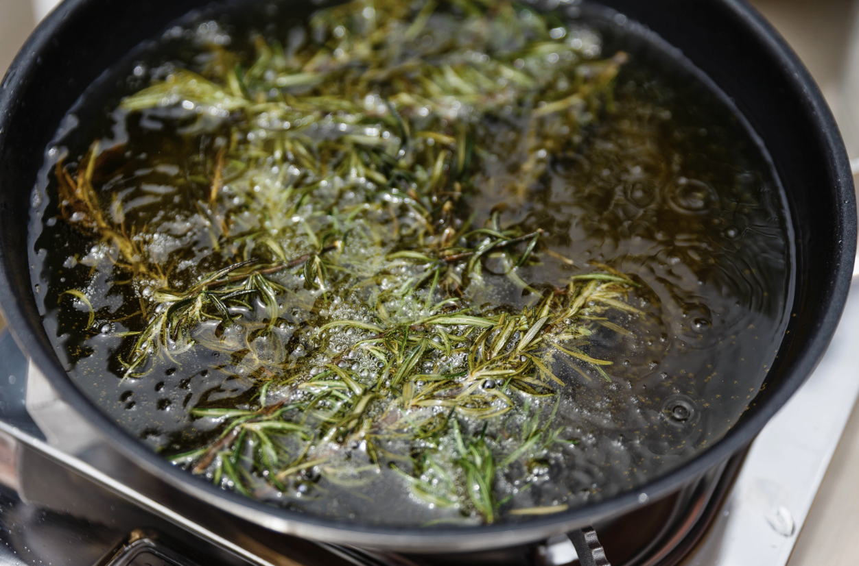rosemary and other herbs steeping in olive oil on stove